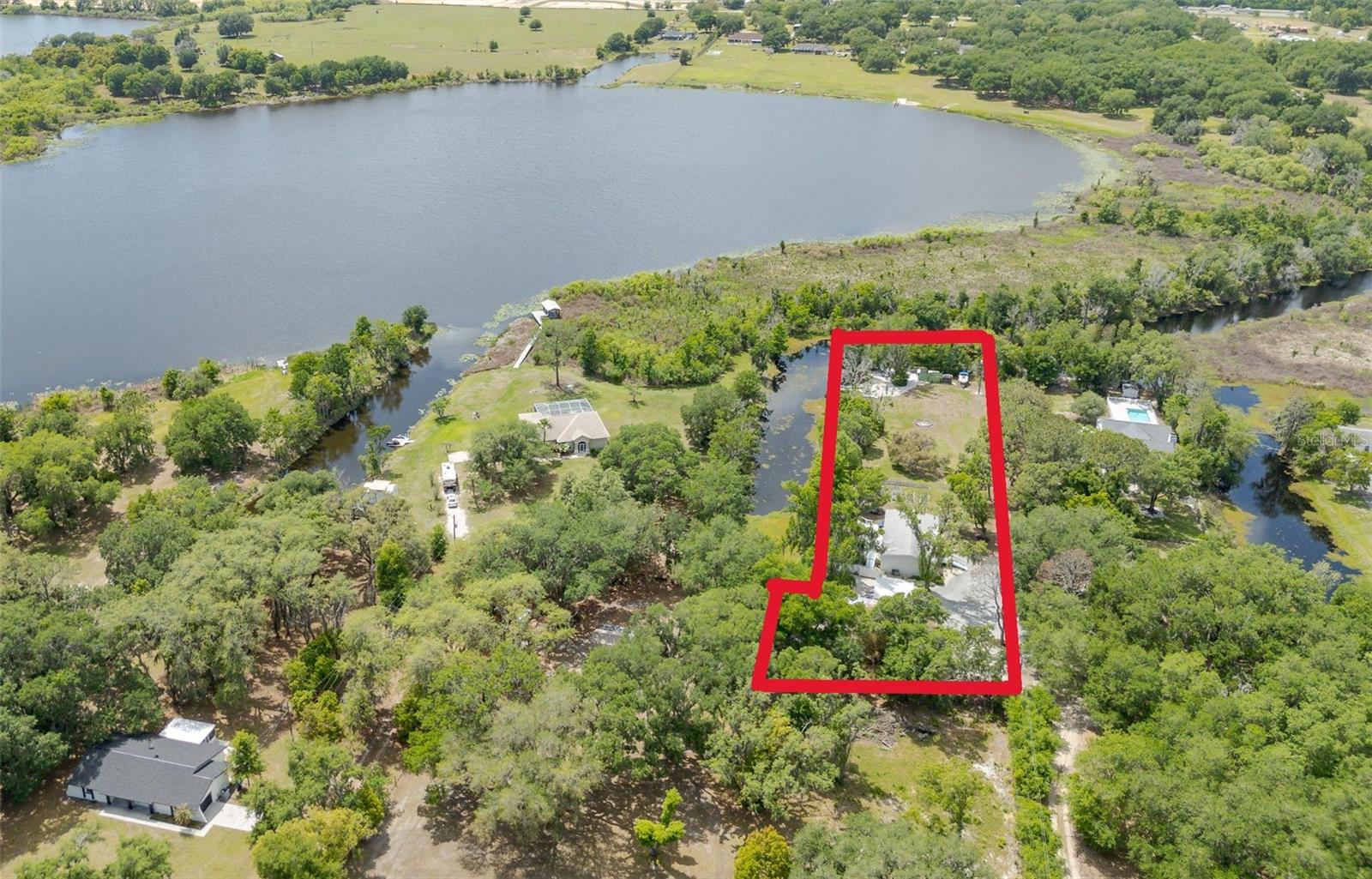 RARE WATERFRONT ACREAGE IN THE HEART OF WESLEY CHAPEL.Truly one-of-a-kind, this exceptional property offers 500 feet of private waterfront with access to a ski-sized lake—an increasingly rare opportunity to own a large, secluded parcel with direct water access in a prime and rapidly growing area. Located at the end of a quiet dead-end road, this LAKE WATERFRONT PROPERTY delivers unmatched privacy while remaining just minutes from top-rated schools, shopping, dining, major highways, and popular destinations like Epperson Lagoon. A unique blend of WATERFRONT LIVING, USABLE LAND, AND LOCATION makes this a standout opportunity for homeowners, investors, or those looking to build a custom luxury estate.The MOVE-IN READY 3-BEDROOM, 2-BATH HOME features an open split floor plan, custom high ceilings, and a spacious kitchen with a large island and oversized pantry. The primary suite offers a garden tub and separate shower, creating a comfortable retreat—ideal for immediate use, rental income, or while planning future development.Step outside and experience TRUE FLORIDA WATERFRONT LIFESTYLE. A 40-foot deck, leading to a 24-foot pier—perfect for fishing, relaxing, or enjoying sunset views. The property also includes a PRIVATE BEACH AREA, canoe and kayak rack, a floating dock with gangway, boat launch, fish feeder, battery charging station, and wash station—fully equipped for boating, jet skis, kayaking, and outdoor recreation.Enjoy outdoor living with TWO DISTINCT FIREPIT AREAS—a tropical-style firepit near the home for everyday relaxation and entertaining, and a second firepit at the beach area with water and electric, creating the perfect setting for evenings by the lake. Or just relax by a BONFIRE under the stars.The PARK-LIKE GROUNDS are rich with natural beauty and wildlife, including sandhill cranes, osprey, hawks, wild turkey, and songbirds, occasional otters—, creating a peaceful, private setting rarely found in this location.This VERSATILE WATERFRONT PROPERTY WITH LAND includes a 20x20 insulated and air-conditioned WORKSHOP/GARAGE with finished interior, welding outlets, airlines, remote compressor connection, and attached restroom. A separate insulated office provides an ideal WORK-FROM-HOME SETUP in a natural environment. Multiple sheds and a leveled FULL RV HOOKUP provide ample space for boats, RVs, Toys and equipment.For those seeking a SELF-SUFFICIENT LIFESTYLE, the property features an irrigated raised-bed garden, vine racks, mature GRAPEVINES, a tool shed, and a spacious CHICKEN COOP.Important updates include a refurbished septic system (2017) and a private well with a new pump and pressure tank (2023). With its combination of 500 FT OF WATERFRONT, ACREAGE, EXISTING INFRASTRUCTURE, AND FUTURE BUILD POTENTIAL, this property presents a rare opportunity to create a CUSTOM LUXURY WATERFRONT ESTATE, hold as a long-term investment, or enjoy as a private retreat.RARE OPPORTUNITY IN WESLEY CHAPEL—properties offering this level of waterfront, privacy, and flexibility are rarely available. This is truly a property that must be experienced in person to fully appreciate its setting and potential. Schedule your private tour today and see why this property stands out. List Agent is owner. Don’t forget to view the video tour!