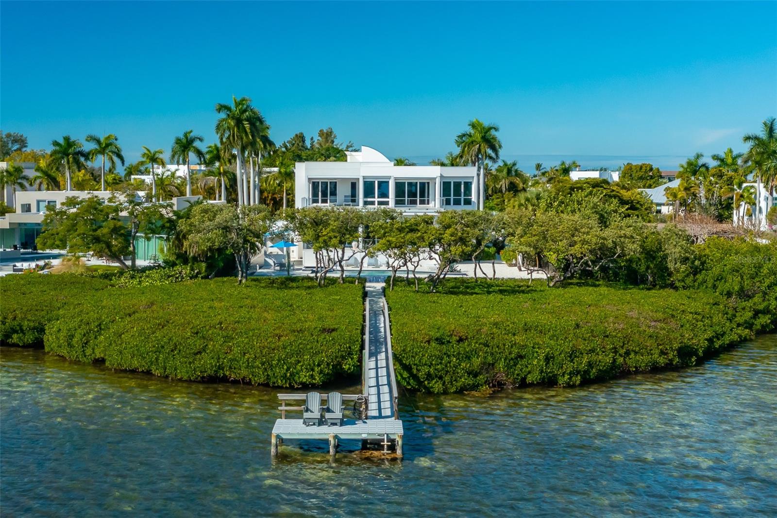 An extraordinary expression of modern waterfront living, this custom-designed Sarasota residence seamlessly blends architectural distinction, refined interiors and a tranquil Bayou setting flowing directly into the Gulf of Mexico, creating a home that is visually striking and effortlessly livable. Thoughtfully conceived by the owners, this exceptional five-bedroom, three full-bath and one half-bath waterfront residence is on approximately .37 acres and was designed to honor its surroundings while embracing contemporary form, function and natural light. Offering 4,284 square feet under air and 6,416 total square feet, the home makes a striking yet calming first impression. A circular brick-paver driveway, decorative architectural elements, trellises accents, curated landscaping, and subtle exterior lighting establish a refined sense of arrival and architectural presence. Inside, a dramatic open-concept floor plan unfolds with intention and volume. The great room features ceilings approaching 20 feet, custom wire railings and expansive glass frame serene water views from every room. Natural materials, most notably warm cedar accents carried seamlessly from interior to exterior, create a cohesive modern design language. Beechwood flooring, refined finishes, automatic solar window treatments, imported European light fixtures, and integrated LED lighting enhance comfort and contemporary appeal. The gourmet kitchen is designed for everyday living and entertaining, featuring Porcelanosa Design cabinetry, a side-by-side paneled Sub-Zero refrigerator, Asko dishwasher, Wolf built-ins including wall oven, warming drawer, microwave, a U-Line under-counter wine cooler, illuminated onyx island, quartz countertops, seamless under-cabinet lighting and a walk-in pantry. A new Whirlpool top-load washer complements the Whirlpool Cabrio Platinum dryer, completing the home’s functional amenities. The residence offers exceptional flexibility with two private primary suites on the main and upper levels, each providing direct terrace access and tranquil water views. Spa-inspired baths, one features a steam shower and walk-in closets, creating serene retreats. Additional guest suites, office, a waterfront gym or flexible living space, and these multiple en-suite accommodations support a variety of lifestyles. Outdoor living is equally compelling. A saltwater infinity-edge pool with spa and planter waterfall feature anchors the waterfront setting, complemented by covered and enclosable lanais with automatic window and terrace screens. Existing posts for the hammock overlook the Bayou. The outdoor pavilion provides space for an outdoor kitchen, with room to add a built-in grill, ice maker or under-counter refrigerator with existing gas hookup and water supply. A private illuminated dock provides direct Bayou access leading into the Gulf of Mexico, enhancing the home’s connection to nature and offering multiple gathering spaces ideal for entertaining and cherished memories. Modern construction, impact-rated openings and integrated smart-home technology contribute to peace of mind and long-term value. In one of Sarasota’s desirable waterfront neighborhoods, with optional deeded Lido Shores beach access and proximity to downtown Sarasota, St. Armands Circle and Longboat Key, this residence offers privacy, elevation, serenity and refined expression of luxury coastal living, designed to be admired and lived in.