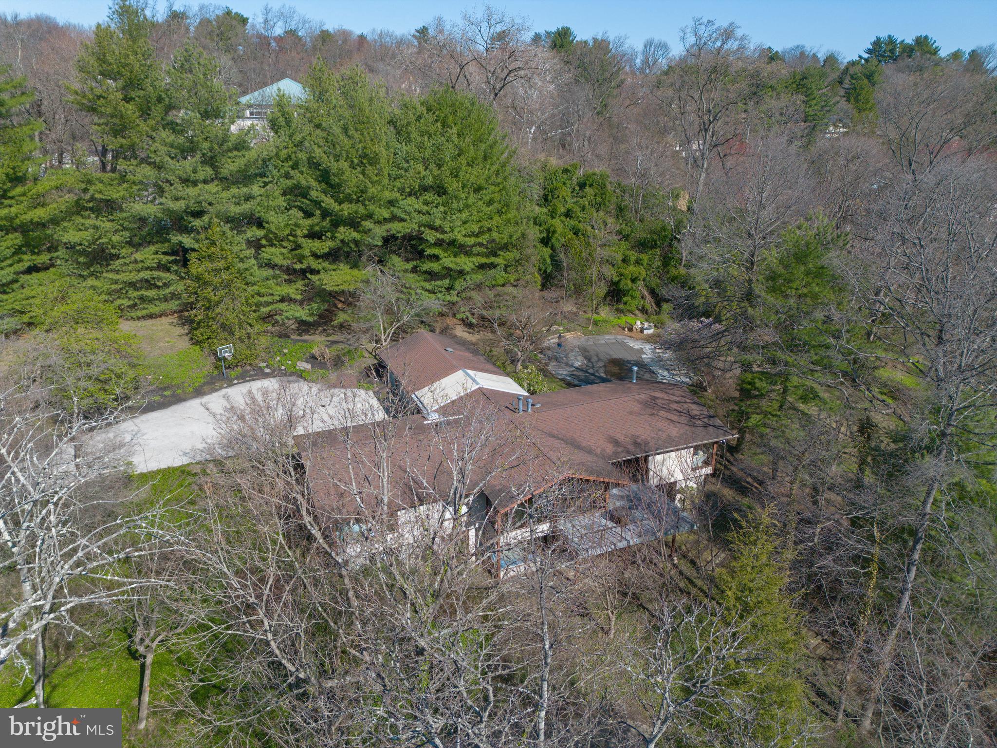 Modern elegance and expansive living spaces define this exceptional six-bedroom estate by renowned builder Robert McElroy, privately set on 3.83 acres and featuring a SEPARATE GUEST HOUSE.Beyond the gated entrance, a long, winding drive leads to a sophisticated yet understated residence highlighted by soaring ceilings, walls of glass, and rich wood accents throughout. A dramatic glass atrium-style reception hall with slate flooring creates a striking first impression. The stunning living room boasts a vaulted ceiling and an impressive window wall, filling the space with natural light and offering serene views of the surrounding landscape.The adjacent dining room, also with a vaulted ceiling and glass walls, provides seamless access to a wraparound deck—perfect for indoor-outdoor entertaining. The gourmet, center-island kitchen is a true showpiece, featuring exotic wood and stainless steel cabinetry, Blue Macaubas granite countertops, honed limestone floors, with premium appliances. Glass doors lead directly to the deck and pool area.A bright breakfast room with floor-to-ceiling windows connects the kitchen and family room, complete with custom built-ins. The main level is further enhanced by a luxurious primary suite offering a private sitting room, walk-in closet, and a sleek, spa-like bath.The lower level includes five additional bedrooms, 2 bathrooms, a laundry room, and a spacious recreation room with multiple windows and sliding glass doors, providing direct outdoor access.In harmony with the main residence, the guest house (built in 1990) offers approximately 1,000 square feet on the upper level, which could be used as a spacious home office with a sink, dishwasher, refrigerator, powder room, and access to a private deck through sliding glass doors. The lower level features an exercise room, full bath with shower, and a one-car garage.Additional highlights include a two-car attached garage, a whole-property generator servicing the home, guest house, and front gate, and beautifully landscaped grounds with mature trees. The resort-style swimming pool creates a private outdoor oasis, ideal for both relaxation and entertaining.A rare offering combining architectural distinction, privacy, and luxury amenities.