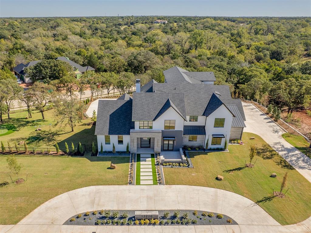 A stunning architectural masterpiece blending contemporary design with timeless materials and cutting-edge technology. The exterior features painted brick, stone, and stucco, complemented by artificial turf landscaping and extensive LED lighting. A circular drive leads to the home, while the rear offers resort-style outdoor living with a granite fireplace and fully equipped outdoor kitchen with built-in burners, refrigerator, vent hood, and marble surround. The 20x40 sports pool features in-floor cleaning jets with smart app control, alongside a custom putting green—perfect for practicing your short game. Inside, 21-foot ceilings soar above white oak floors and a dramatic Venetian plaster fireplace. A custom walnut wall with integrated LED lighting adds warmth and sophistication. The chef’s kitchen features a Venetian plaster vent hood, professional-grade appliances, and a hidden back kitchen with gas cooktop, sink, ice maker, and dishwasher—ideal for entertaining. The dining area includes a built-in walnut hutch and a glass-enclosed, temperature-controlled wine room. The office offers a private club feel with white oak walls, black ceiling, and custom bar, opening to a stone patio. The primary suite features acoustic LED wall panels and a micro-cement bath with walk-in shower, soaking tub, floating granite shelving, and walnut cabinetry. The walk-in closet includes custom built-ins and ladder access for seasonal storage. Additional highlights include a mother-in-law suite, powder bath, spacious laundry, three-story elevator, and third-floor retreat with kitchenette, hardwood floors, and panoramic Lake Arcadia views. Smart home automation, integrated lighting and sound, and luxury finishes throughout