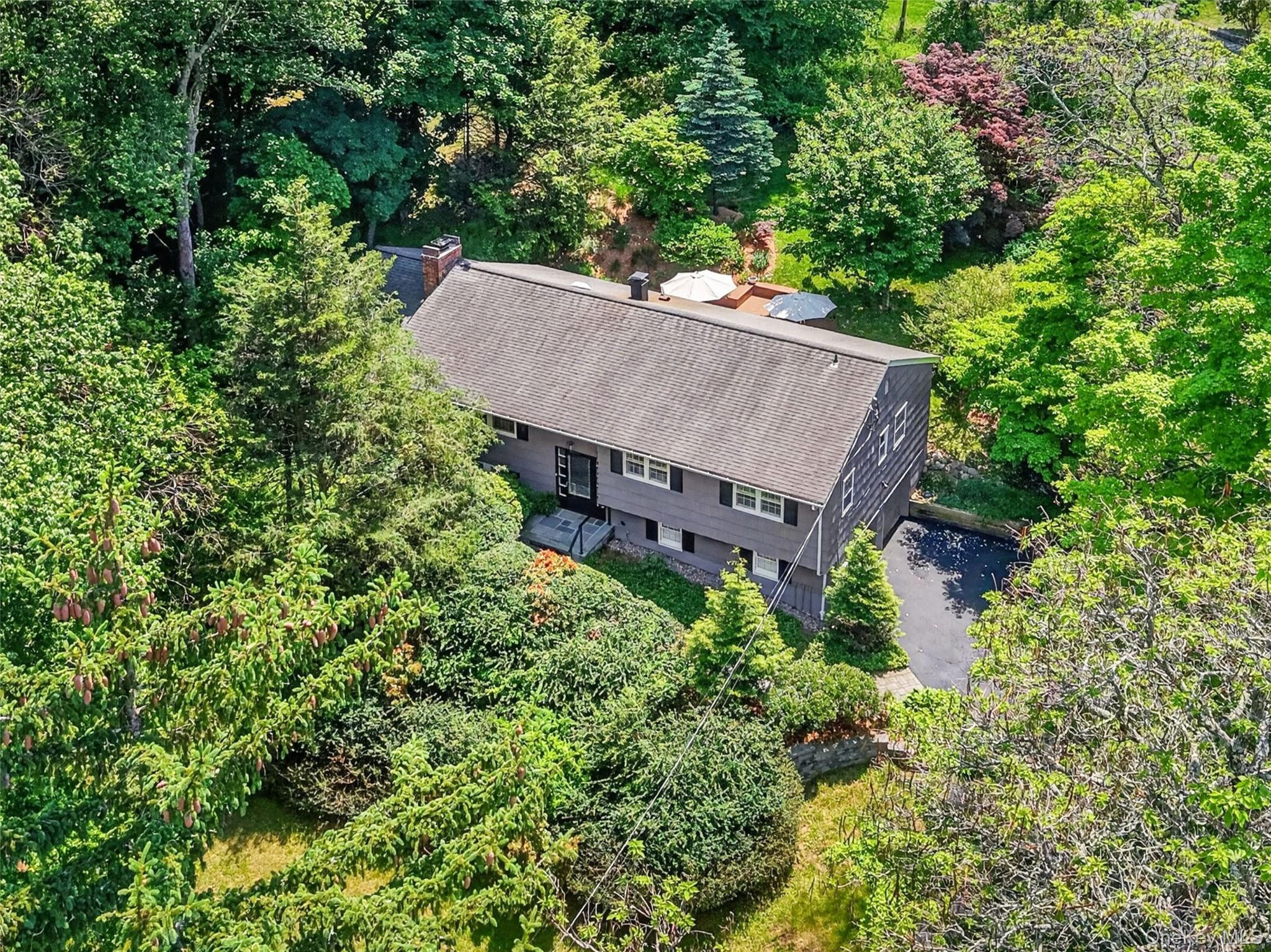 Sun filled and beautifully maintained, this spacious ranch-style home offers comfort, warmth, and a private setting surrounded by nature.  Hardwood flooring flows throughout the main level, featuring a large living room and formal dining room highlighted by a custom double-sided fireplace with custom built-in shelving. A skylight and walls of windows fill the dining room with natural light, while sliding glass doors lead to the expansive deck, creating a seamless flow for indoor and outdoor entertaining. The updated, upgraded and uplifting kitchen features a large center island with seating, cooktop, double wall oven, glass storage cabinets, and double sliding glass doors to the deck overlooking the landscaped shy one-acre sanctuary withdelightful gardens throughout the seasons. The main level offers four bedrooms and two beautifully updated full bathrooms, including a primary bathroom with shower and a hall bathroom with tub. The lower level features laminate flooring and offers additional flexible living space with a family room behind French glass doors, office or den, storage, utilities, and a half bathroom, along with access to the two-car garage.Recent improvements include a new front walkway and steps, adding to the home’s curb appeal. Tucked away in a private setting, yet conveniently close to everything, this special property is located just 1.2 miles to Metro-North and offers easy access to major highways. Enjoy nearby shops, restaurants, golf, hiking, recreation, and activities along the Hudson River. Pride of ownership is evident throughout this lovingly cared-for home.