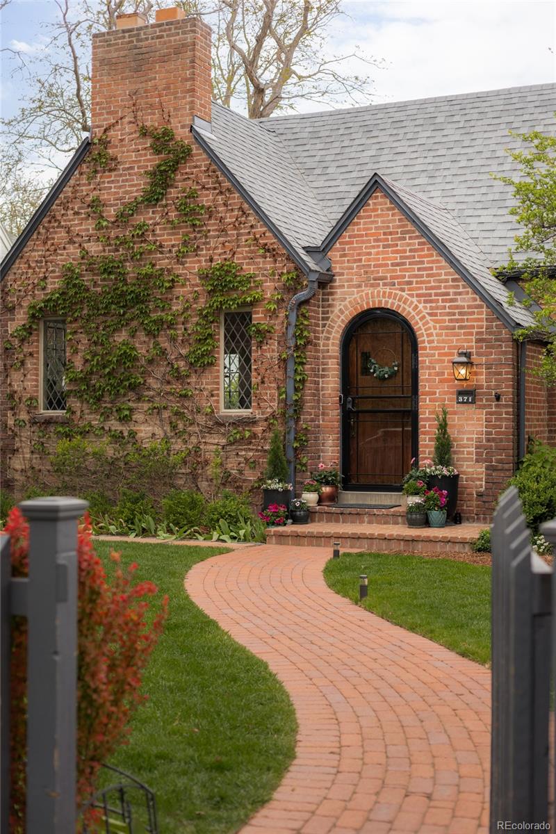 Timeless Tudor elegance meets a masterful modern expansion in this enchanting Hilltop residence. Set on an oversized, tree-lined lot, this home captivates with lush new front and backyard landscaping, a fenced front yard and storybook curb appeal enhanced by a brick walkway, flagstone paths and curated lighting. Inside, refined living and dining spaces showcase a fireplace and designer fixtures, while a European-inspired kitchen stuns with new walnut cabinetry, premium appliances and bespoke finishes. A 2024 addition introduces a luxurious primary retreat on the main level with vaulted ceilings, custom beams, a stone fireplace, spa-caliber bath and an exceptional walk-in closet, plus a mudroom, butler’s pantry and private office. The main level offers three bedrooms, while the finished basement features a rec room, wet bar and extensive storage. The backyard is a true private oasis, thoughtfully designed for both relaxation and recreation. Lush, expansive gardens create a serene setting, complemented by two inviting patio spaces perfect for entertaining or quiet evenings outdoors. Additional highlights include a sport court, tranquil fountain, and a detached two-car garage, all combining to offer an exceptional outdoor living experience. Recent upgrades include new windows (2026), Brand new AC unit and condenser for main home (2024), tankless water heater (2024) and roof (2017).
