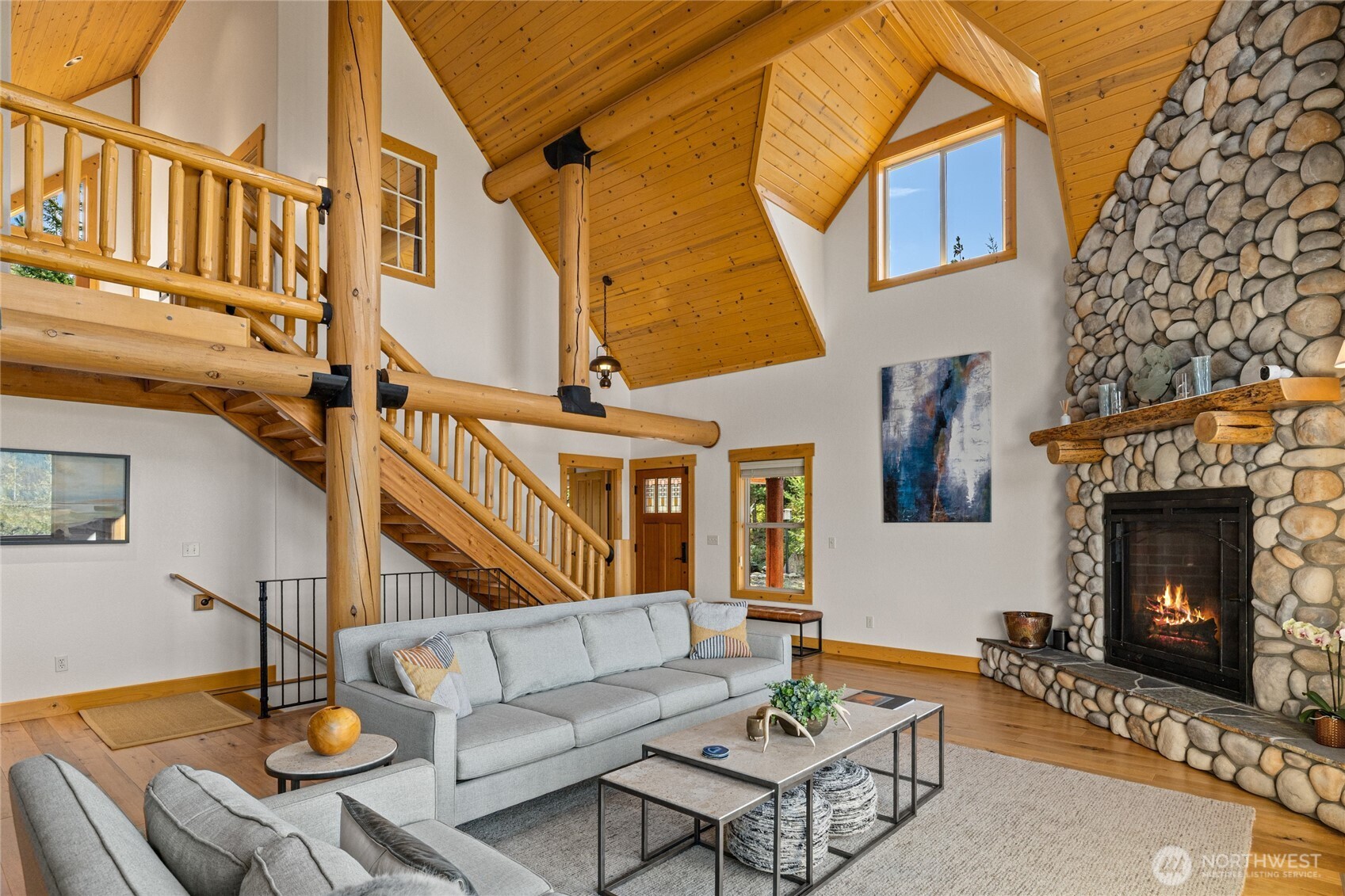 Soaring vaulted ceilings, exposed log beams, and a dramatic floor-to-ceiling river rock fireplace anchor the light-filled great room.