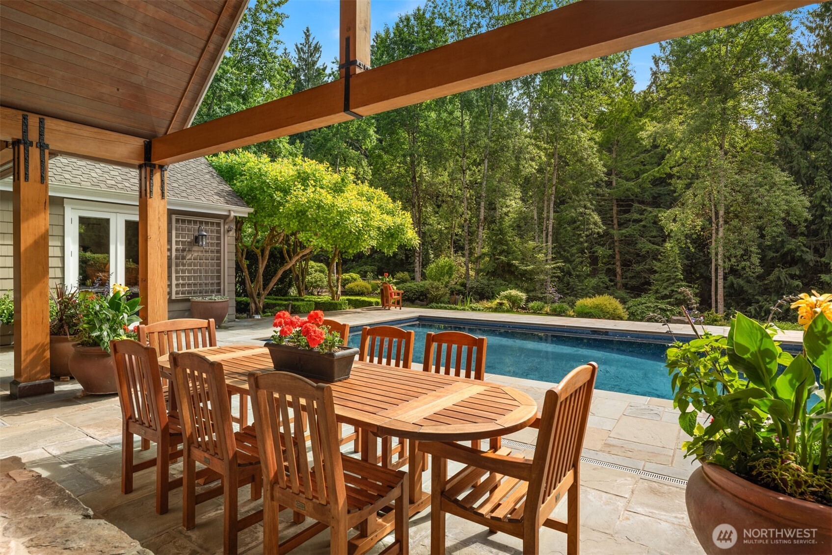 Covered patio with wooden dining table, chairs, and pool view
