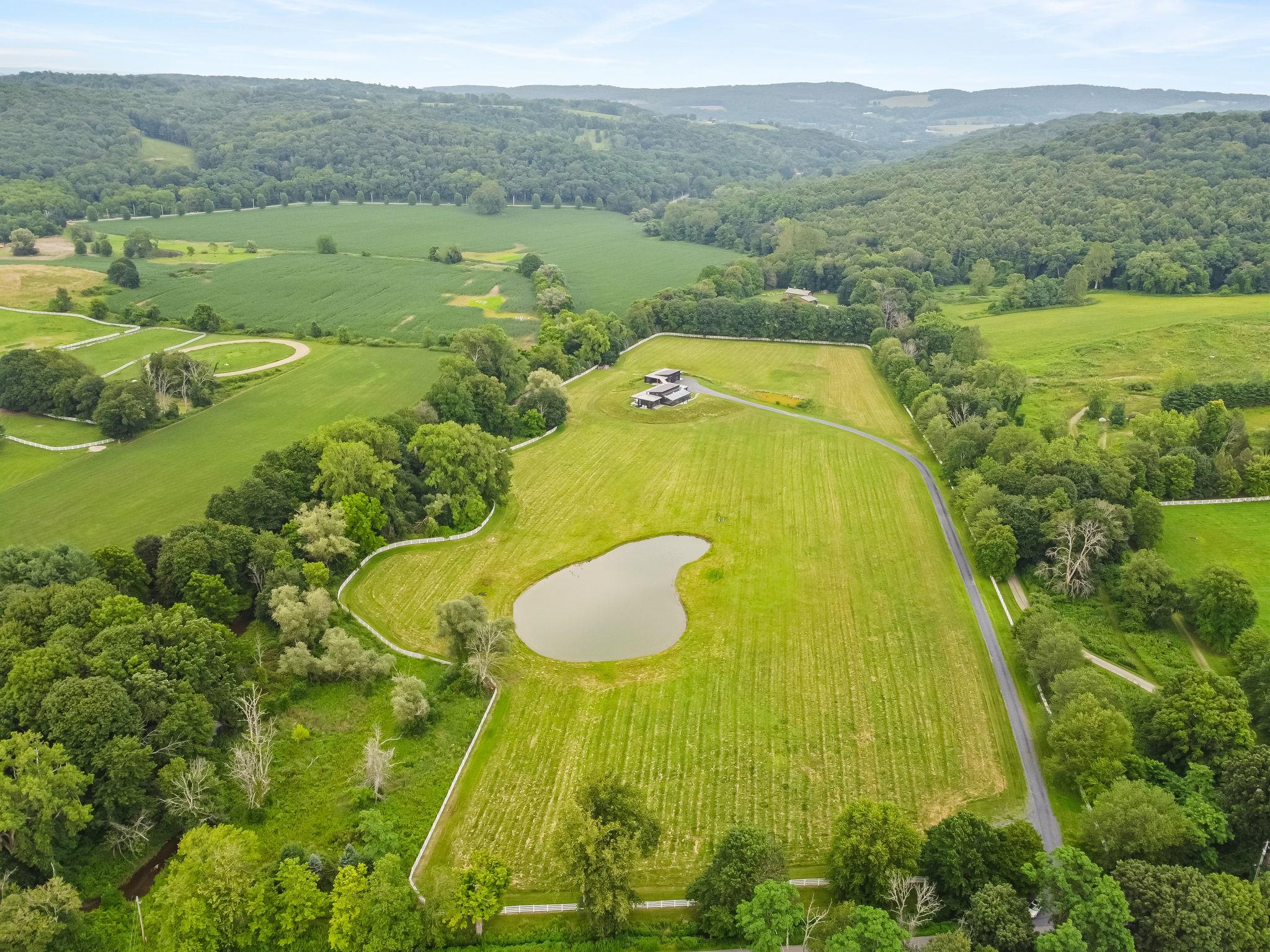 Modern Minimalist Masterpiece on 19 Bucolic Acres in Dutchess County. Welcome to a rare offering in the heart of the Hudson Valley, where striking modern architecture meets timeless pastoral beauty. Completed in late 2024, this extraordinary estate sits on over 19 acres of flat, fenced farmland at the picturesque intersection of Bethel Cross and Carpenter Hill Road. Perfectly sited on a south-facing rise along the Shekomeko Creek, this newly constructed home is a serene, sophisticated sanctuary just two hours from New York City. A bold fusion of modern, industrial, and eclectic design, the residence offers over 4,700 square feet of light-filled, open-concept living on one level, including 3,057+/- sq ft main house, a stunning 1,046+/- sq ft attached greenhouse-conservatory that brings year-round indoor-outdoor living to life and a 1,423 sq ft +/- heated garage/studio/guest apartment. Every detail was curated with intention; from yaki sugi siding and a metal Kemper roof to polished concrete floors and walls of glass that frame unspoiled views of nature. The heart of the home features a bespoke chef's kitchen with live-edge shelving, custom cabinetry milled from trees on the property, concrete countertops, a butler's pantry, and a beverage bar. Double primary suites offer en suite wood burning stoves, spa-like baths with cast iron tubs, Italian tile, and handcrafted metal vanities. Both are complimented by airy bathrooms with natural light and industrial fixtures.A gas fireplace in the ample living room, vaulted ceilings, clerestory windows, and art lighting throughout create a harmonious blend of warmth and style. This is a home designed not just to live in, but to live fully. Outside, the entire 19-acre estate is bordered by classic white 4-board oak fencing, ensuring both privacy and visual continuity. A one-acre, 10-foot-deep pond and expansive flat pastures make this a dream property for equestrians, polo enthusiasts, hobby farmers, or anyone seeking a deep connection with the land. Zoned as a horse farm within an agricultural district, it offers rare potential for animal lovers and breeders alike.
Car collectors and creatives will appreciate the oversized, fully heated garage and studio space outfitted with track lighting, storage, and the flexibility to serve as an art gallery, workshop, or one-bedroom apartment. With a 3,000 sq ft unfinished basement, covered porches, multiple patios, and estate management partners already in place, the property is as functional as it is inspiring. Additional features include an Endless Pools heated performance pool in greenhouse. The home has a sustainable, passive solar design and was constructed to allow for a future living roof/rooftop deck. New well, septic, and underground utilities. Energy-efficient systems throughout. Surrounded by horse farms and wildlife. Just minutes from the town center and Mashomack Polo Club.
Whether you're an artist, gardener, equestrian, or collector, this unique Hudson Valley estate delivers a modern lifestyle without compromise. Offered for the discerning buyer seeking privacy, sophistication, and natural beauty in equal measure.