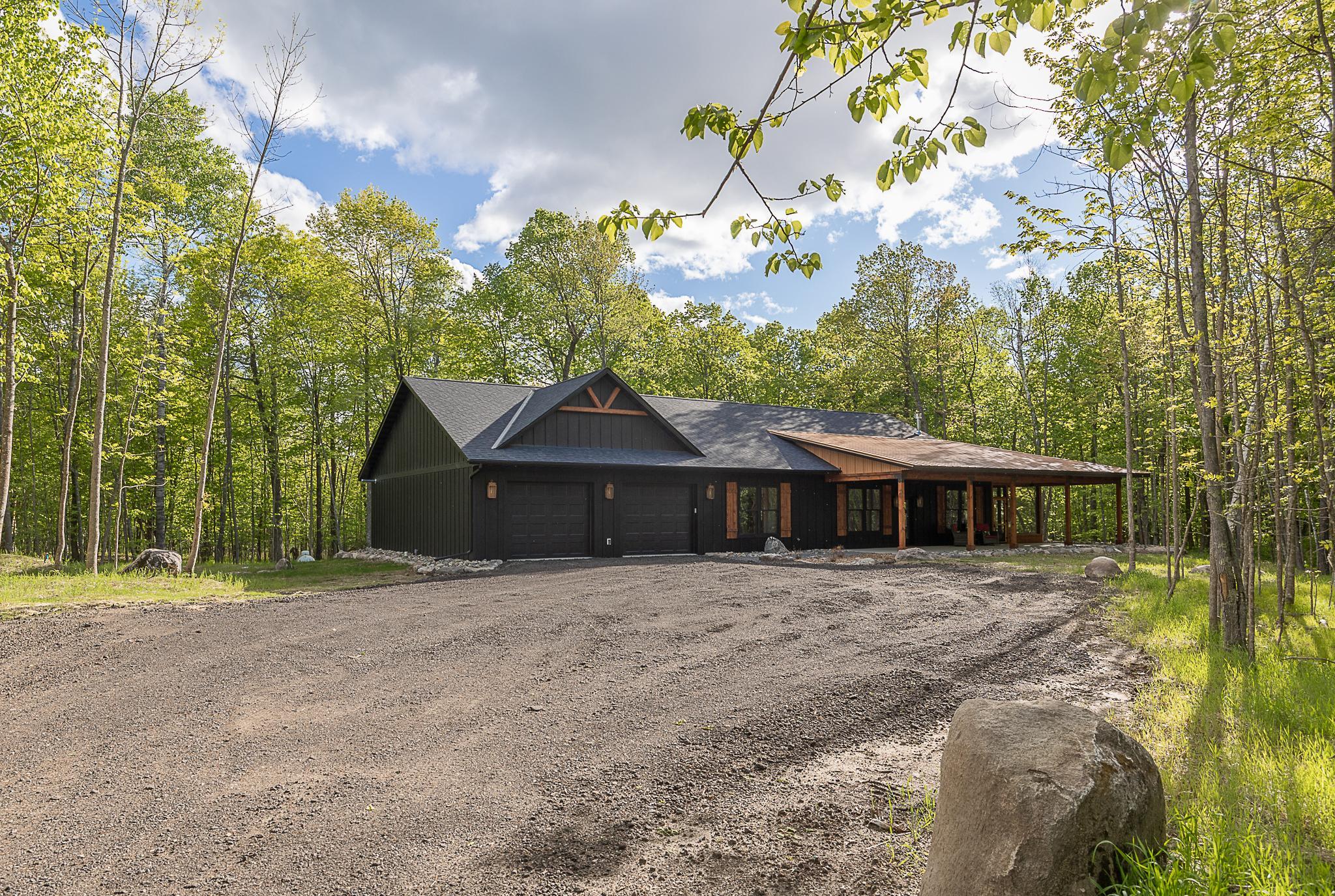 Tucked into a serene, wooded setting on 2.37 acres, this beautifully crafted 3-bedroom, 2.5-bath home offers the perfect blend of rustic charm and modern comforts — with coveted access and a slip on Girl Lake, part of the scenic Woman Lake Chain. A spacious, covered front porch welcomes you to this newly built retreat, where natural wood ceilings, warm wood floors, and thoughtful design details create an inviting atmosphere throughout. The vaulted, beamed ceiling unites the open-concept kitchen and living area, centered around a stunning stone gas fireplace with a built-in space for your TV. The kitchen is as functional as it is stylish, featuring Quartz countertops, a gas stove, ample island seating, a large walk-in pantry, and a custom side table ideal as a buffet, serving space, or even a home office setup.
The primary suite is a true retreat with a walk-in closet and private en suite bathroom. Two additional bedrooms are connected by a spacious Jack-and-Jill bath, while a third powder room provides added convenience for guests. Step out to the large screened-in back porch and enjoy peaceful views of the surrounding woods — the perfect spot for morning coffee or quiet evenings. This home combines the beauty of nature with lake lifestyle living — ideal as a year-round residence or tranquil getaway. With access to Girl Lake and the broader Woman Lake Chain, your waterfront adventures await just steps from your door.