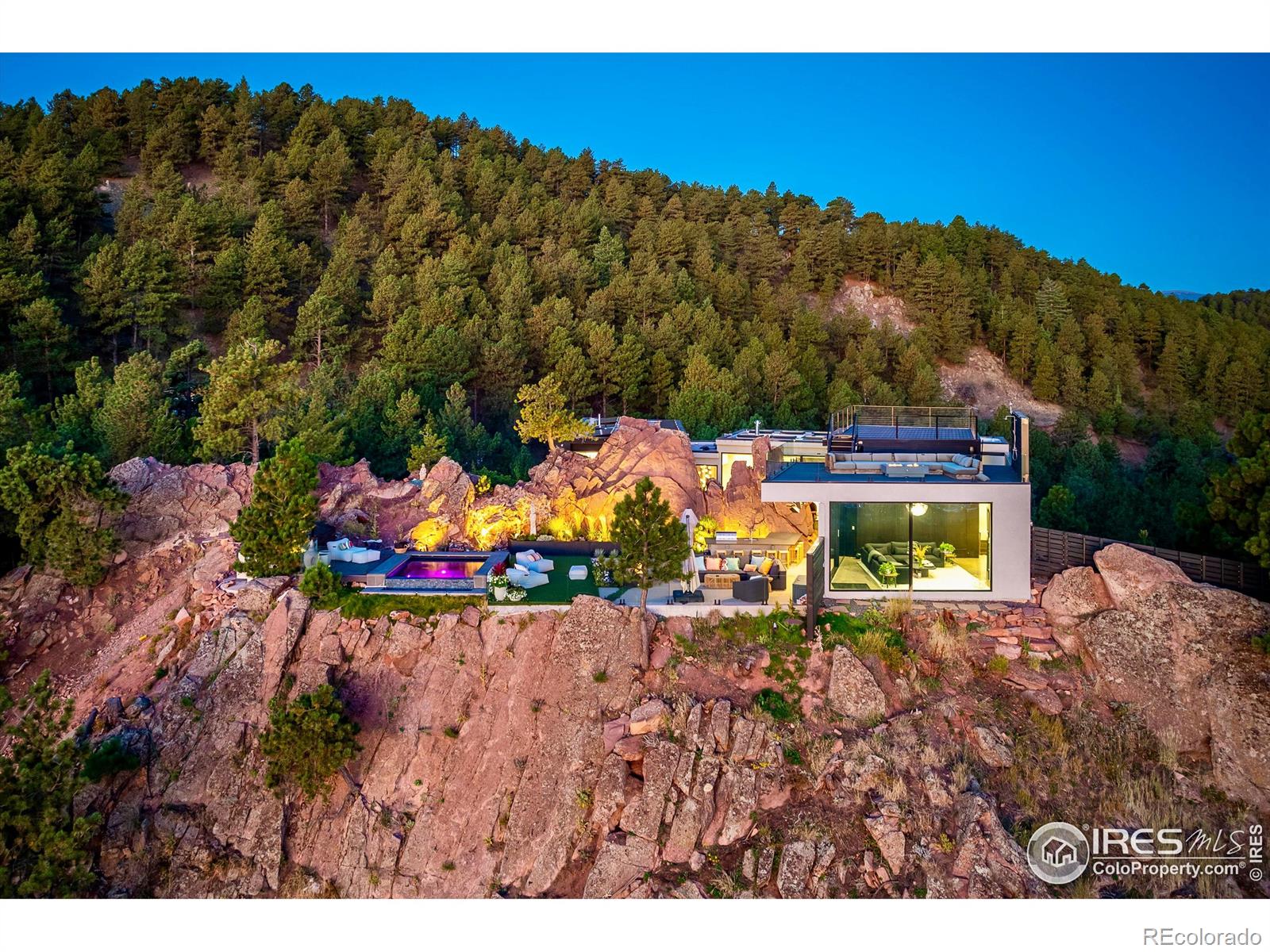 Nestled into the sandstone cliffs of Pine Brook Hills and offered for the first time since construction, 1151 Timber Lane is a bold architectural statement fusing modern design with Colorado's natural beauty. Conceived by Adam Oklesh Architects, this 5-bedroom, 5-bathroom residence captures panoramic east and west views while offering exceptional privacy and outdoor amenities. Set on 2.44 acres, the 4,348-square-foot home features soaring ceilings, floor-to-ceiling windows, and sophisticated natural finishes including rift-sawn white oak and stone. Radiant floor heating and energy-efficient, fire-rated materials ensure long-term comfort and resilience. The great room, anchored by a sleek fireplace, flows into the chef's kitchen with vaulted ceilings, luxury appliances, striking marble island, and breakfast nook connecting to the dining area. The private wing includes a luxurious primary suite with spa-like bath and walk-in closet, two additional en-suite bedrooms, and a flexible fourth bedroom or office. A fifth bedroom suite offers ideal guest or studio space. Expansive sliding glass doors lead to two outdoor sanctuaries. The main terrace features a fire pit, built-in grill and outdoor kitchen, oversized bar seating, outdoor heaters, and a dramatic infinity-edge pool floating above Boulder valley. The west-facing flat yard offers a sunlit retreat surrounded by rock outcroppings, mature trees, and custom Marpa landscaping. The rooftop deck provides unforgettable sunrises, sunsets, and stargazing with views stretching from the Flatirons to city lights and the Continental Divide. Additional features include an attached 2-car garage with generous storage and elevator access throughout. Experience Boulder living at its finest; luxurious interiors, architectural significance, unmatched outdoor spaces, and jaw-dropping 360-degree views in a one-of-a-kind retreat just 6 minutes from Broadway and 12 minutes from downtown Boulder.