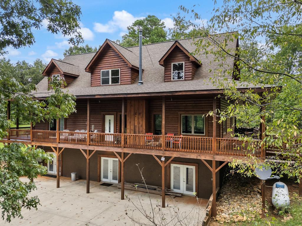 Tucked away on nearly 7 acres of unrestricted wooded land with no HOA, this stunning 4-bedroom, 3 full bath, 2 half bath log-sided cabin offers the ultimate privacy, freedom, and rustic charm. A long private driveway winds beneath a canopy of hardwoods, leading to a welcoming home wrapped on all four sides by a wide covered porch with an 80' ramp, and to enjoy every angle of this stately home. Step inside your foyer, with locally sourced marble floor - the very same marble that's on the Cherokee County courthouse! - and into the expansive Great Room, where wood ceilings, warm heart-pine wood floors, and a cozy wood-burning stove framed by a tile hearth to create a true mountain lodge feel. The open kitchen impresses with an oversized island, abundant cabinetry, open shelving, and a bold red retro-style refrigerator. The main level also features a convenient half bath with marble floor, laundry with sink, and the first of THREE MASTER SUITES with dual walk-in closets, private porch access, and a spa-like bath with tiled shower, garden tub, and marble floor. Upstairs are a second bedroom, a bonus room, and two additional Master Suites with ensuite baths. The lower level expands the possibilities with a partially finished recreation room, two sets of glass doors to a patio, a half bath, and another large bonus room with outdoor access. Whether you envision a private mountain retreat, short-term rental, or forever home, the unrestricted land gives you endless options—add a garage, build a workshop, bring your RV, or simply enjoy peace, seclusion, and the freedom to make this mountain property your own. And with high-speed Fiber Optic internet, you're always connected!  Call us today for more details, pictures, and maps of the property.