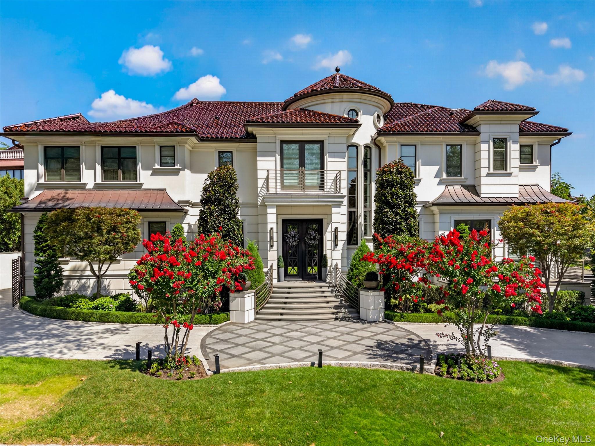 Custom Mediterranean-Contemporary Estate !!!An extraordinary opportunity to own a one-of-a-kind Mediterranean-Contemporary estate in desirable Bayside. Built in 2021, this architecturally distinctive residence offers approximately 5,144 sq. ft. and is set on an exceptional 100' × 100' / 10,000-sq.-ft. property, delivering remarkable scale, privacy and resort-style living rarely found in Queens.The striking exterior showcases a classic red-tile roof, elegant architectural detailing, contemporary metal railings, balconies and beautifully manicured landscaping. Inside, a dramatic double-height foyer immediately establishes a sense of grandeur with floor-to-ceiling windows, custom wall paneling, expansive marble-look flooring and a sculptural curved staircase. Above, a rotunda-style ceiling with dimensional detailing and cascading statement chandelier creates an unforgettable architectural centerpiece.The breathtaking double-height great room features exposed beams, an open second-floor gallery and a soaring fireplace feature wall anchored by a distinctive double-sided indoor/outdoor fireplace. Architectural metal-and-glass doors, designed to complement the dramatic front entry, bring abundant natural light into the space and create a seamless connection to the covered outdoor lounge, where the opposite side of the fireplace serves as an equally impressive focal point.The adjoining designer chef's kitchen features extensive custom cabinetry, sleek countertops, an oversized center island with generous seating, designer pendant lighting and a professional-grade multi-burner range beneath a striking metal hood and metallic backsplash. A separate pantry/service area provides additional cabinetry and workspace. A sun-filled breakfast area and elegant formal dining room with herringbone wood flooring, geometric coffered ceiling and statement chandelier complete the main entertaining spaces.Upstairs, the open gallery overlooks the foyer and great room. The expansive primary suite is a private sanctuary featuring custom ceiling treatments, a separate sitting area and spa-inspired bath with freestanding soaking tub, oversized glass-enclosed shower, dual vessel sinks, makeup area and illuminated architectural details. A beautifully designed walk-in dressing room offers extensive built-in cabinetry, shelving, hanging space, drawers and center storage.The exceptional lower level is conceived as a private entertainment and wellness retreat, featuring an expansive media lounge, dedicated recreation and billiards area, and a beautifully appointed private fitness studio. A bespoke hospitality-inspired bar and lounge offers generous seating, illuminated display shelving, beverage refrigeration, sink, rich wood detailing and brick accents, creating the ambiance of an exclusive private club.Outdoors, the estate transforms into a private resort, centered around a resort-style saltwater pool with elevated spa, expansive terraces and mature privacy landscaping. The covered alfresco living and dining pavilion features architectural ceiling detailing, fans, television and the outdoor face of the home's dramatic double-sided fireplace, creating an inviting open-air living room. A fully equipped outdoor culinary pavilion offers multiple cooking stations, sink, extensive cabinetry, generous preparation surfaces and bar seating.Completing this exceptional residence are an expansive second-floor rear terrace, a meticulously finished attached garage and thoughtfully designed indoor-outdoor living throughout.A truly distinctive Bayside estate combining grand architecture, sophisticated design, exceptional entertaining spaces and resort-style amenities on a rare 10,000-sq.-ft. property.