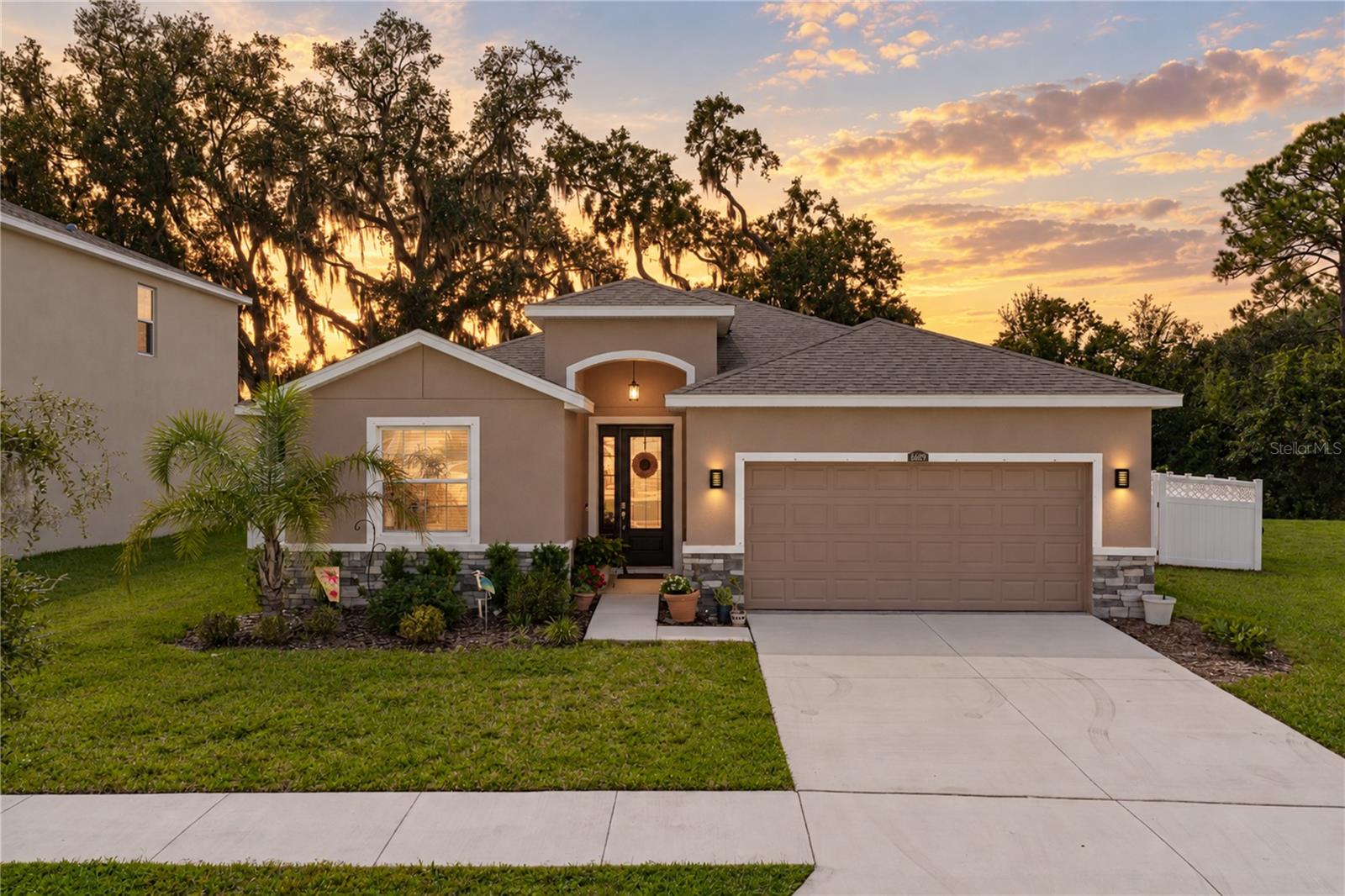 Imagine unwinding on your oversized covered patio, looking out across the backyard to a beautiful treelined landscape. Built in 2022 within the established Silverado Ranch community, this 4 bedroom, 2.5 bath, 2 car garage home features 2,046 sq ft of living space, a thoughtfully arranged split bedroom plan, and a picturesque outdoor setting that makes coming home something to look forward to! Sidewalk-lined streets, tropical landscaping, attractive stone accents, and a covered entryway welcome you to this beautifully maintained residence. Inside, neutral tile flooring extends throughout the main living areas, leading into an expansive 13x22 living room with triple sliding glass doors that showcase the backyard and provide direct access to the covered patio. The open layout keeps the dining room and kitchen within view, making the main living area feel connected and inviting. Granite countertops, stainless steel appliances, and a generous central island with breakfast bar seating make the kitchen a wonderful place to prepare meals while staying connected with family and guests. A walk-in pantry provides plenty of additional storage, while the neighboring dining area features a ceiling fan for added comfort. A conveniently located half bathroom in the hallway is an appreciated addition when entertaining. Privately separated from the secondary bedrooms, the primary suite is a relaxing retreat with plush carpet flooring, 2 spacious walk-in closets, and an ensuite bathroom featuring dual granite-topped sinks, a walk-in shower, a separate soaking tub, and a private water closet. Near the front of the home, bedrooms 2 and 3 are comfortably positioned on either side of the second full bathroom. Bedroom 4 enjoys its own separate location, making it a fantastic option for overnight guests, a craft room, or a dedicated home office. The generous backyard has been thoughtfully fenced to preserve one of the property's most appealing features: the view! Privacy fencing along the sides provides separation from neighboring properties, while vinyl picket fencing across the back keeps the scenery beautifully visible. The oversized covered patio gives you plenty of room for outdoor dining, comfortable seating, and afternoons in the shade, while the fenced lawn creates a wonderful place for pets and play. Just a short distance away, Silverado Ranch residents can enjoy the community clubhouse, resort-style swimming pool, playground, and swing set. Located in an established Zephyrhills neighborhood with convenient access to Wesley Chapel, Downtown Zephyrhills, and Dade City, this home makes it easy to enjoy the surrounding area while having a welcoming place to return to each day. Call today to schedule your private showing!