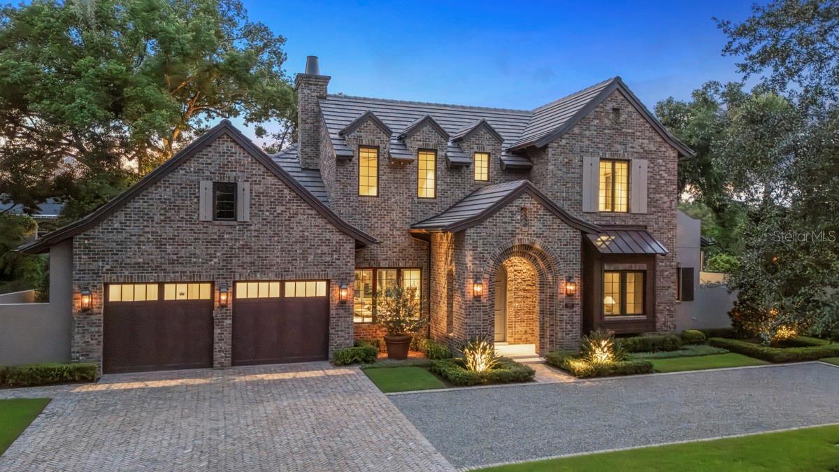 Welcome to 702 Via Bella, an impressive 2025 English cottage estate by Floridian Custom Homes that captures the essence of timeless architecture exemplifying elegance and artisan craftsmanship. In one of Winter Park’s desirable residential corridors, warmth and beauty abound in this four-bedroom, six-bath residence spanning 3,720 square feet or air conditioned and 4,535 square feet total under roof, offering layered living, artisanal materials, and a modern infrastructure. Upon entry through a solid mahogany front door, warmth and beauty abounds with Botticino limestone flooring enhanced by a textured finish, extensive custom millwork, and an abundance of open concept living areas. Coffered ceilings and recessed WAC lighting create a gallery-like ambiance, enhanced by natural light from insulated casement windows. The central living space integrates with the dining area and designer kitchen, which features custom cabinetry by Grit & Grain, leathered Taj Mahal quartzite surfaces, and chef-grade appliances: a La Cornue 43-inch gas range with McGurken hood, Thermador 30-inch refrigerator and freezer columns, and Bosch dishwasher. The kitchen transitions into a walk-in pantry with cabinetry, quartzite, dual refrigeration drawers, and a dedicated ice maker. An oversized mudroom, finished with hardwood built-ins, offers expanded storage and functionality. The first-floor primary suite is privately positioned in its own wing and finished with wide-plank European white oak flooring by Forrest Accents, a walk-in closet with textured built-in systems, and a spa bath with natural stone countertops, Rohl polished nickel fixtures, a marble-tiled floor and shower, and a frameless glass enclosure. All doors are solid core with Emtek hardware. The library, near the front of the home, offers a quiet retreat with matching oak floors and custom casements. A solid wood staircase leads to the second level living areas including a lounge flex space. There are three additional bedroom suites, each with en-suite baths, which offer porcelain flooring, frameless glass shower doors, brushed quartz and dolomite vanities, decorative lighting, and built-in closet systems. Additional features include CAT-5/6 wiring, Sonos-integrated speakers, lighting automation via the Lutron RA-3 smart system, and pre-wired home security with digital camera ports at key access points. Thoughtfully placed access points from the primary suite and kitchen wing lead to a fully enclosed backyard retreat, where mature landscape design by Signature Landscape frames a private outdoor living sanctuary. A Roman-inspired cabana with grand ceilings and exposed beams anchors the outdoor entertaining space, flanked by a fully tiled ($50,000 upgrade) saltwater pool featuring therapy jets, LED-lit bubblers, a dual-skimmer system, automated controls via a Jandy heat pump, and a Paramount self-cleaning system. Clay brick pavers and landscape lighting define the walkways as well as front entry driveway. This home was constructed with stem wall foundation, concrete block first-floor exterior walls, and 2-by-6 second-floor framing for structural performance along with spray foam and sound mat insulation between floors ensure comfort and acoustic separation. Finished in a palette of clay brick and hand-troweled stucco, the home is crowned with architectural tile shingles and custom metal accents. Eight-inch half-round gutters, aluminum downspouts and engineered drainage ensure long-term performance.