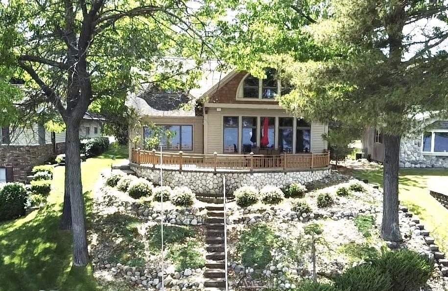 This truly exceptional home was designed to showcase not only the gorgeous water and wooded scenery, but to do so with quality, comfort, and style. Thoughtful details are reflected throughout. Expansive Andersen windows bathe the home in natural light while framing captivating lake views. On the main floor, the open concept great room with its soaring stone fireplace and wood cathedral ceiling share custom wood floors and panoramic water views with the adjacent kitchen & dining area. At the heart of the well appointed kitchen is a generous granite island with plenty of counter seating. Stainless steel appliances, a walk-in-pantry, custom cabinetry and door leading to the lakeside patio deck are featured as well. Gathered around the staircase, the spacious primary bedroom with en-suite bath enjoys first floor living along with the den/bedroom, laundry/mud room, and second bathroom. At the top of the stairs is a curved overlook offering a bird's eye view out to the lake and main floor below. Two additional large bedrooms and a bathroom complete the second level. Step out onto the lakeside stone deck/patio to enjoy the vista of all sports Van Etten Lake. Gently terraced paths and steps lead to the lakefront complete with your own private dock, boat hoist, beach house and fire pit. In addition to the attached garage there is a 2+ detached garage (22x 36) to provide storage for all your gear, toys, ATVs, vehicles. The home is being offered turn key-fully furnished-with a few minor personal exclusions. This property provides everything you need for year round living or a get-a-way retreat. As a real plus, adding to the value of the home and years of care free living, the owners are scheduling installation of a new three dimensional shingle roof on the house and attached garage. This is an unbeatable package on a great inland lake!!!