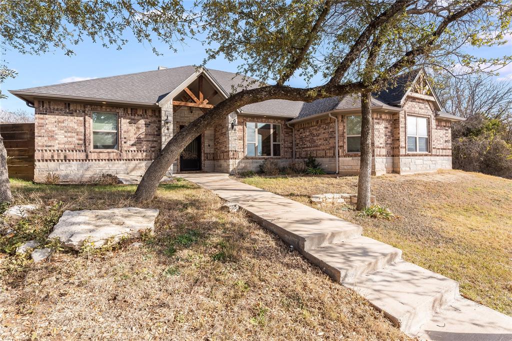 Situated high at the end of a quiet cul-de-sac, this brick and stone home offers privacy, views, and convenient access to the amenities Pecan Plantation is known for. Inside, tile plank flooring extends through the main living areas, complemented by crown molding, arched doorways, and neutral paint colors that create a comfortable, cohesive feel throughout. The open-concept living, kitchen, and dining areas are anchored by a floor-to-ceiling stone fireplace, providing a natural focal point for both daily living and entertaining. The kitchen features knotty pine cabinetry, granite countertops, a center island with breakfast bar seating, ample prep space, and a walk-in pantry. A spacious dining area completes the layout, well-suited for gatherings of any size. The primary suite is generously sized and positioned for privacy, with two additional bedrooms and a full bath located across the home. With ample guest parking, this home is well suited for hosting friends and family. Located within the gated community of Pecan Plantation, residents enjoy 24-hour security and a wide range of amenities including championship golf, multiple swimming pools, tennis and pickleball courts, dining options, a car wash, and a full-service grocery store—all within the community.