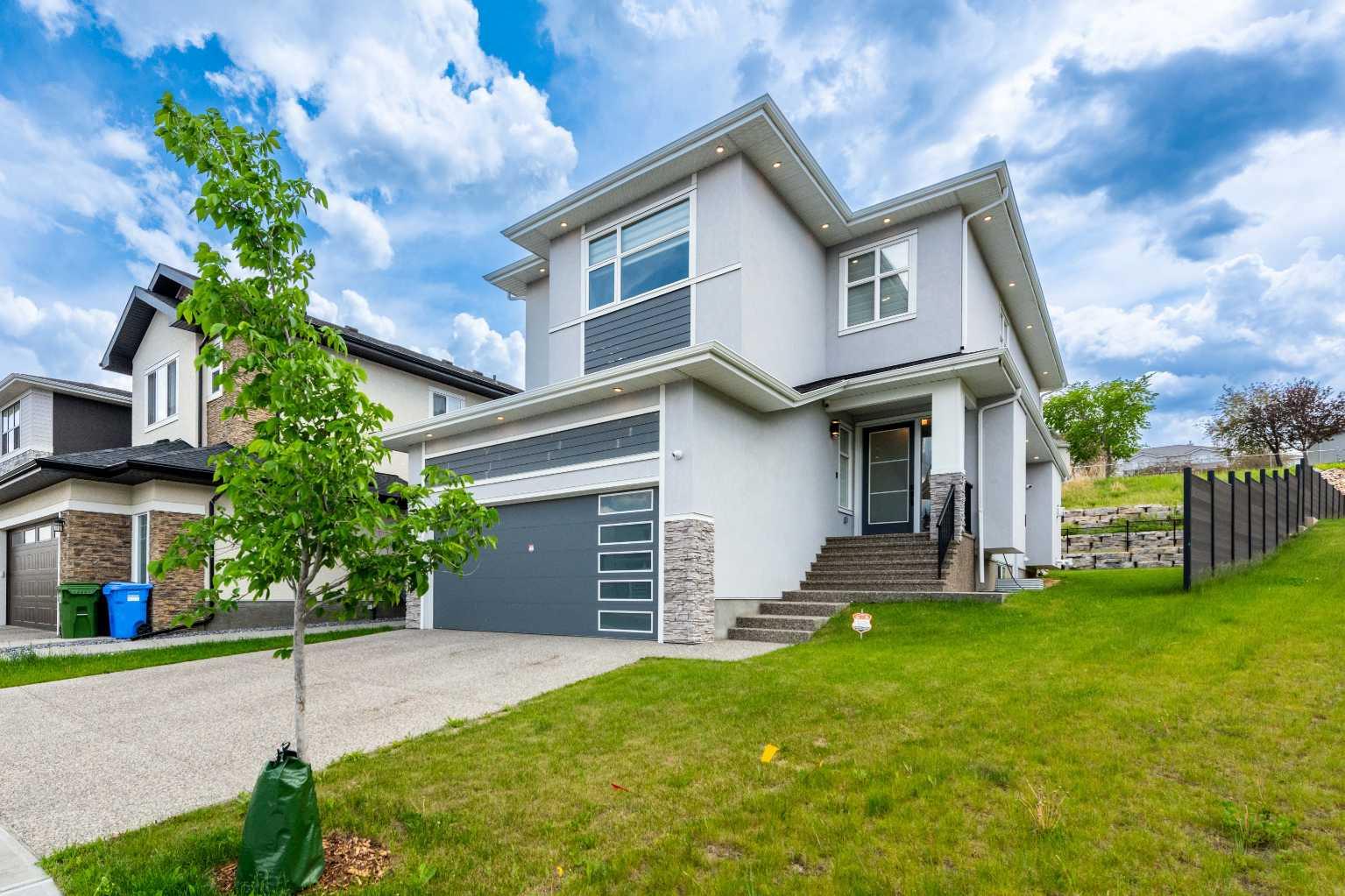 Welcome to this fully upgraded 6-bed executive home, built in 2022 on a PIE-SHAPED lot located on a quiet cul-de-sac in The Hamptons—one of Calgary’s top golf course communities. With over 3,400 sq. ft. of living space, this home blends luxury, comfort, and smart design. As you enter, you’ll be impressed by the grand open-to-below formal living space with large windows, high ceilings, engineered hardwood floors, 8-foot doors, and modern glass railings. The main floor is bright and open, featuring a spacious living room with a sleek fireplace, a formal dining area, and a dream kitchen with premium KitchenAid appliances, shaker cabinets, quartz countertops, a large island with undercounter vacuum system , and a walk-through pantry. There’s also a versatile den or office that can be used as a bedroom, along with a full bathroom—perfect for guests or multigenerational living. High-end finishes and 9-foot ceilings on all three levels enhance the upscale feel. Upstairs offers 3 spacious bedrooms and 3 full bathrooms. Generously sized master suite with tray ceilings, a huge walk-in closet, and a spa-like ensuite featuring heated floors, jacuzzi tub, double undermount sinks and custom shower. A second master bedroom with its own ensuite adds convenience and flexibility. A third bedroom with a full bathroom, bonus room and upper-level laundry with a sink complete this floor. The fully finished basement has a separate side entrance and includes two large bedrooms, a full bathroom, a cozy rec room with a big wet bar—great for entertaining. Outside, enjoy a south-facing fully landscaped backyard that backs onto green space and opens to walking trail for easy access along with added privacy and peace. Extras include built-in sound system on all 3 levels, central A/C, high garage ceilings, motorized window blinds, 80 gallon hot water tank, water softener, hard-wired CCTV camera system and 200 Amp power service. Don’t miss this rare chance to own a custom luxury home in one of Calgary’s most desirable communities. Book your private showing today!