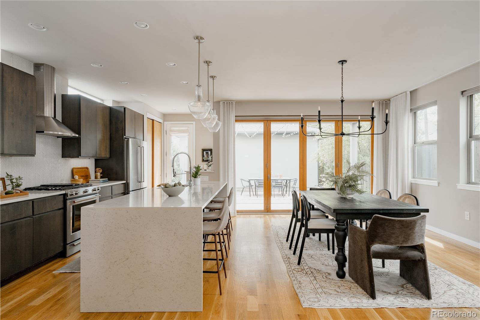 Perfectly poised in the heart of Berkeley, this exceptional 2016 custom-built home by G.J. Gardner is a masterclass in thoughtful design, style, & effortless livability. Rarely does a layout feel intuitive—where every space flows, balancing openness with purpose, function & elevated design. The expansive main level unfolds beautifully with a wide open floor plan anchored by an oversized living room, generous dining, and a stunning gourmet kitchen designed for gathering. Floor-to-ceiling windows flood the home with natural light, while design-forward window treatments and timeless finishes create a sophisticated atmosphere. A spacious main-floor office offers the ideal work-from-home retreat, tucked thoughtfully away from the primary living spaces. Upstairs, three generously sized bedrooms, all on one level, provide comfort and privacy, while the home’s five baths are beautifully appointed with enduring, high-quality finishes, three of which have heated floors. The finished basement is exceptional—offering a secondary living and entertainment space complete with projector, bedroom, and an enormous storage room. Crowning the home is a spectacular rooftop studio and lounge space with wet bar- perfect as a gym, creative studio, secondary office, or inspiring retreat. From this elevated perch, take in sweeping mountain views and unforgettable sunsets. Outside, the home is equally captivating. An enchanting English-inspired lilac garden welcomes you from the front, perched gracefully above the street for both privacy and presence. The mature landscaping and accordion doors blending indoors and out create multiple destinations to entertain, dine, stargaze, or simply enjoy quiet Colorado evenings under the open sky. Oversized 2-car garage is the finishing touch to this incredible property. All of this, just moments from the vibrant shops, restaurants, and neighborhood energy of Tennyson Street and Highlands Square—offering the very best of Berkeley living at your doorstep.