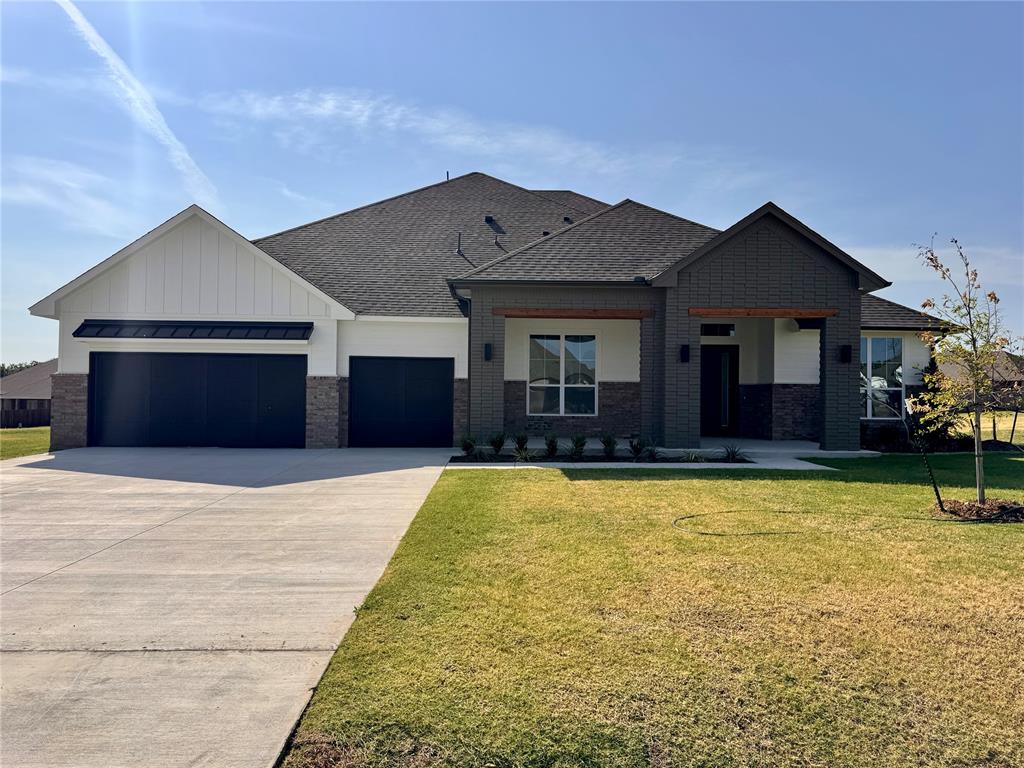 This new construction home offers approximately 3,042 square feet with four bedrooms, three-and-a-half bathrooms, and a three-car garage. The floor plan includes a wide entryway leading into an open living area. Wood-look tile flooring is planned throughout the main living spaces. The living room features a stone-tiled fireplace, a large wood mantle, and oversized windows. The kitchen includes soft-close custom cabinetry, thick quartz countertops, a large island with a farmhouse sink and built-in trash drawer, floating shelves, stainless steel Samsung built-in appliances, a decorative vented hood, and a walk-in pantry. Additional interior spaces include a study with built-ins, a powder room, a flex room, and a utility room with cabinetry and a sink. The primary suite layout includes a spacious bedroom and a bathroom with dual vanities, a vanity desk, a walk-in shower, a freestanding soaking tub, and a large walk-in closet with natural light. The covered back patio is planned with gas and TV hookups. Energy-related features listed for this plan include a 96% efficient tankless water heater, radiant barrier roof decking, low-e Thermalpane windows, insulated and sealed ducts, multiple insulation components, and an Ecobee3 Lite thermostat. Construction details include engineered foundation review, exterior brick with stone accents (per elevation), Atlas HP42 shingles, Tyvek HomeWrap, structured wiring, and various mechanical and safety features. The home is located on a half-acre (mol) lot in a community that allows outbuildings. Access to HWY 9, I-35, and I-44 is noted.