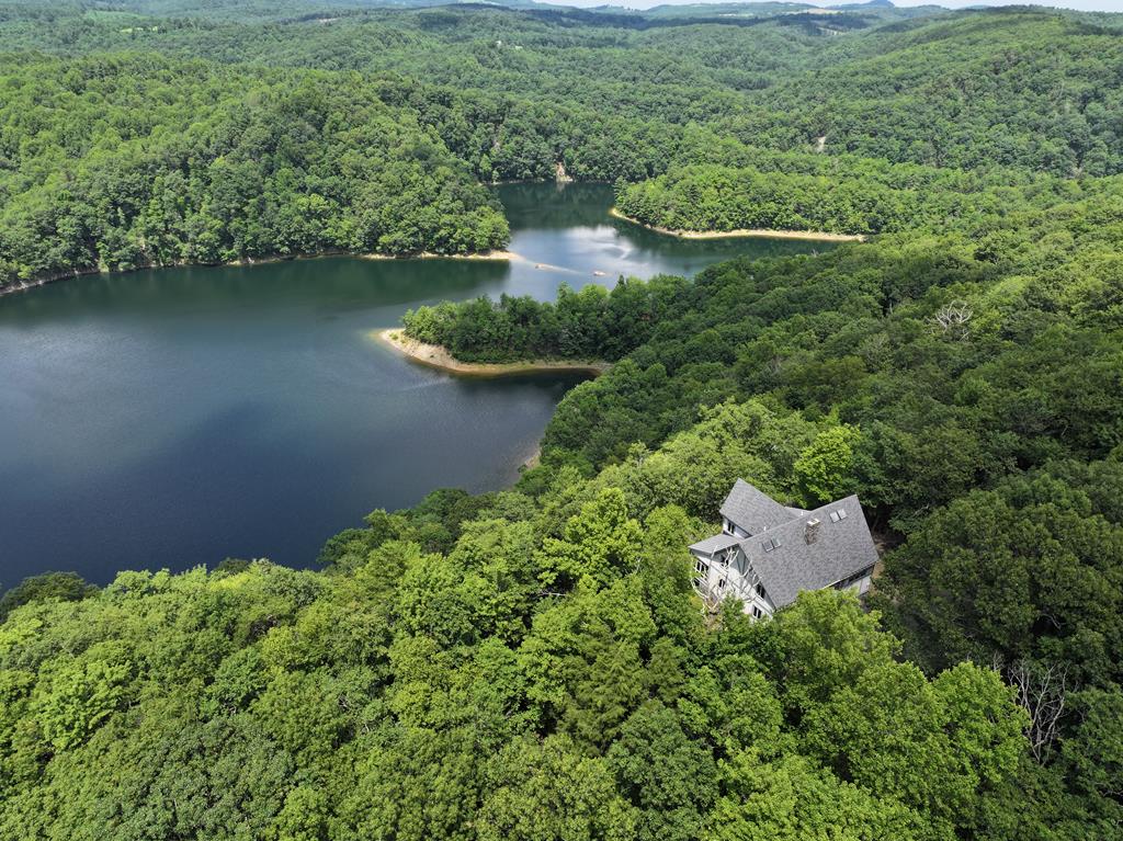 Stunning Contemporary Home with Panoramic Dan River and Reservoir Views on 11.5 acres. Welcome to 191 Reservoir Overlook, an impressive 4-5 bedroom, 4.5-bathroom contemporary retreat in Swiss Chalet style. It offers 3,952 sq ft of beautifully finished living space on 11.5 acres in the serene Meadows of Dan, VA. The home itself contains the sturdy and traditional craftsmanship of Virginia timber framers. Located within the breathtaking surroundings of the Primland Auberge Resort Collection – but not part of the resort – this property provides privacy and freedom along with accessibility to resort amenities' golf & restaurants. The home includes Wi-fi capabilities, central heat, spring water, gas fireplace with remote, and the main floor's heated tile flooring. Step into the foyer leading first to a room with versatile possibilities as a bonus bedroom, office or TV room with convenient half bath. The main floor features the heart of this home to be an open living room with unique hand stacked stone fireplace reaching up through the center of home's soaring cathedral ceiling of pine wood beams. Seamlessly connected is an open kitchen and dining area, both maximizing the stunning vistas of Talbott Reservoir and the Dan River. Enjoy peaceful mornings or sunset evenings in the expansive, glass enclosed sunroom which adjoins the living room, dining  room and primary bedroom suite, all offering panoramic views, creating an atmosphere of true relaxation. The luxurious primary bath with garden style tub & heated tile floors completes this private sanctuary. Upstairs, and also offering scenic views, is a bright loft area, ideal for reading or lounging, alongside two spacious bedrooms, each with its own sky lights and full bath for ultimate guest comfort. The finished walk-out basement offers a fourth bedroom; a large area perfect for family gatherings, game room or media space; a full bath; laundry room; and a well-equipped workshop for hobbies or projects.