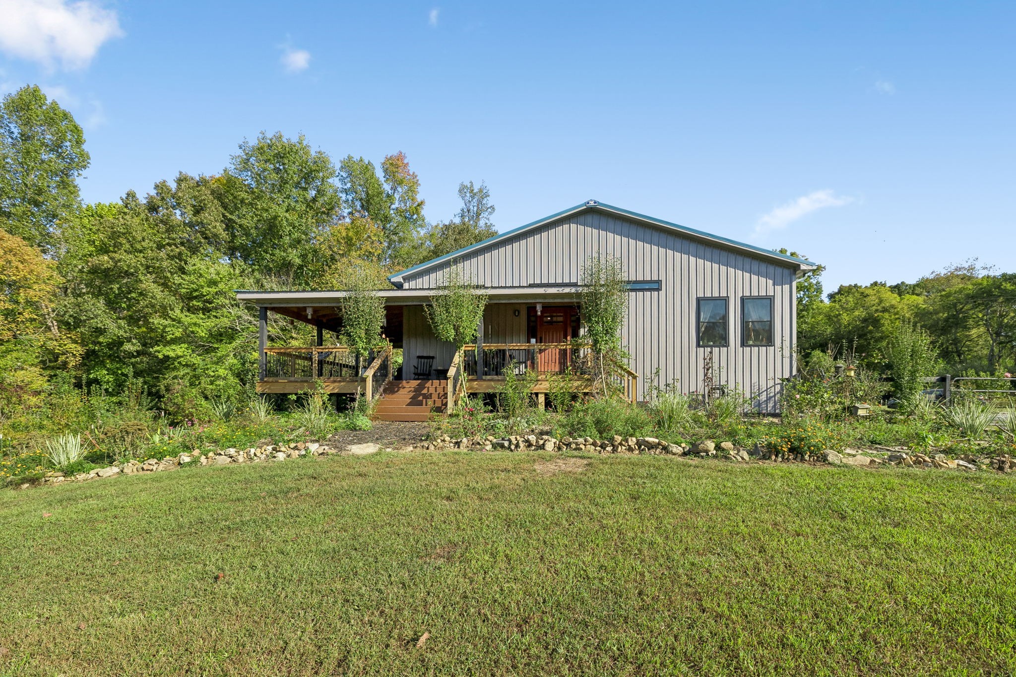 Country living meets modern convenience on 10.2 acres in Hurricane Mills! Completed around 2022, this custom 3BR/2BA barndominium offers approximately 1,600 sq. ft. of main living space, peaceful views, a beautiful mix of open and wooded land, serious workshop space and private guest accommodations with NO HOA. Inside, enjoy 3/4-inch solid hickory hardwood floors, an inviting open living area and a cook's kitchen with oversized island, 36-inch range, commercial-style hood, pot filler, granite countertops and full-height backsplash. A walk-in pantry, separate wet bar with granite backsplash and dedicated office behind sliding farmhouse-style doors add function and charm. The guest bath features a jetted tub, separate shower and antique vanity. All appliances, including washer/dryer, convey. Additional comforts include on-demand hot water and double-hung windows. The attached approx. 1,200-sq.-ft. 3-car shop/garage is a standout, with 14-ft ceilings, 10-ft-wide door, 100-amp subpanel, abundant workbench outlets, dual-basin sink and urinal. An approx. 250-sq.-ft. guest loft features its own mini-split HVAC, shower, toilet and sink, ideal for visitors or flexible space. Closed-cell spray foam insulates the entire building, including walls and roof. A natural-gas 22kW Generac whole-house generator provides backup power. 1-Gig fiber internet and extensive CAT6 wiring make working from home easy. Outside, enjoy the covered porch, expansive L-shaped Trex deck reinforced for a hot tub, fenced yard and fruit orchard. Dedicated RV parking offers 50-amp electric, water and sewer hookups. An insulated 12x16 well/pump building has its own 50-amp service. Well water, city sewer and two additional sewer taps on the rear acreage offer future flexibility, subject to approvals. Peace, privacy and possibilities for days!