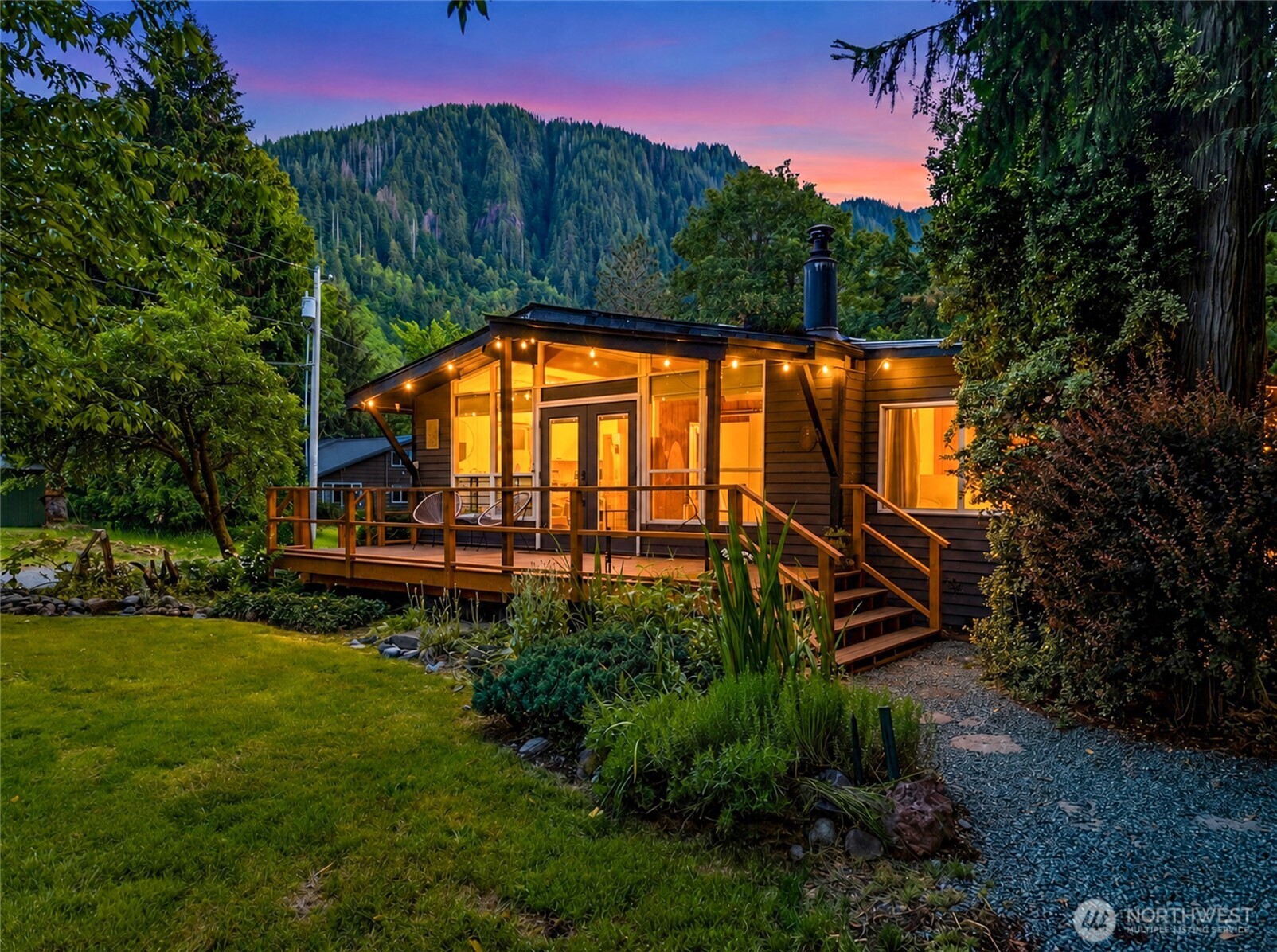 Escape to the Cascades in this beautifully updated mid-century mountain cabin nestled beneath towering evergreens at the base of majestic Mt. Baring in a riverfront community just 20 minutes from Stevens Pass. Unwind in the covered hot tub, gather around the firepit beneath the stars, or enjoy the grassy yard and tree swing beneath the apple tree while taking in the soothing presence of the nearby Skykomish River. Inside, vaulted ceilings, abundant natural light, warm wood accents, a cozy woodstove, and a classic cast-iron soaking tub create the perfect blend of vintage character and modern comfort. Whether you're escaping for the weekend or working remotely for the season, high-speed fiber internet keeps you connected without sacrificing the mountain lifestyle. Extensive updates have enhanced both form and function, including a new roof, mini-split heating and A/C, fresh interior and exterior paint, an updated kitchen, stylish tile, and much more. Multiple outbuildings provide flexibility for storage, hobbies, and mountain gear. Offered fully furnished and turnkey, this proven vacation rental has generated close to $60,000 in annual income, making it an ideal personal retreat, full-time residence, or investment opportunity. Just over an hour from Seattle, this is mountain living at its best.