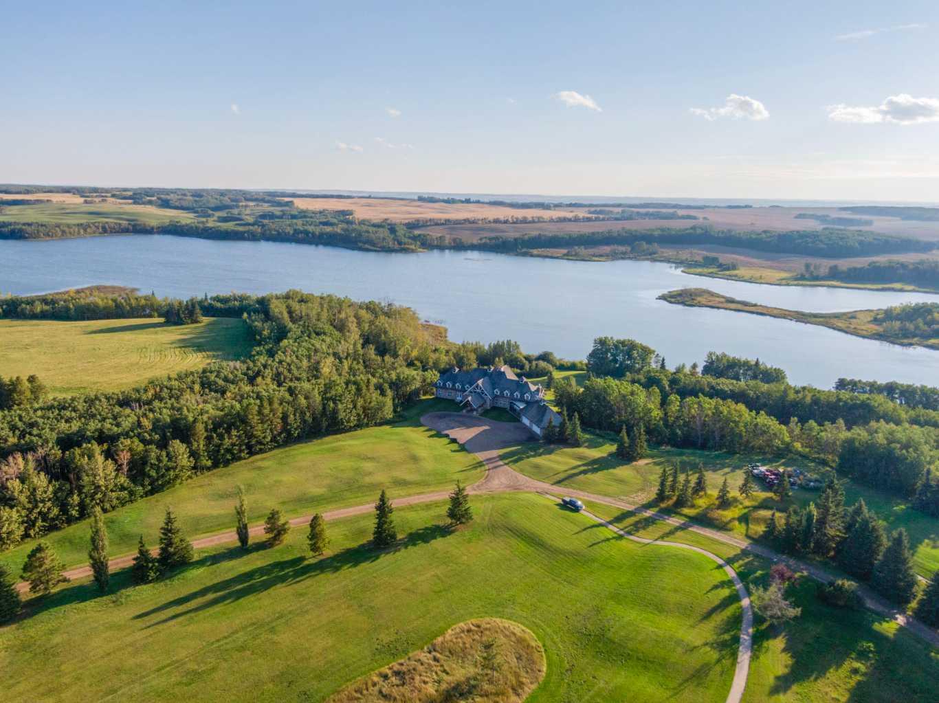 Located in the quiet, picturesque countryside of Lacombe County, the Gadsby Lake Estate is a once in a lifetime opportunity to own a secluded paradise offering just about everything you can dream of. Opulent architectural features and exquisite design elements are found throughout both the main residence and adjacent lodge, including the use of one-of-kind building materials from around the world. In addition to the 17 bedrooms and 31 bathrooms, this stunning estate boasts several specialty rooms including a library, a bright and airy atrium, a sauna and gym, large wine cellar, an indoor pool and lounge, a grand party room, private theatre, and games room. Each space is impeccably designed with elegance, comfort, and convenience in mind. Beautiful windows and outdoor seating lounges, deliver both spectacular lakefront views, and a feeling of tranquility and connection to the serene natural surroundings. Gorgeous stone fireplaces, rich wood accents, and suite-style guest quarters with spa-like ensuites create a warm, welcoming environment for owners and guests alike. A multitude of recreational amenities just for you can be found throughout the Estate’s almost 300 acres. Hiking, fishing, canoeing, and  tennis courts are just some of the activities that can be enjoyed in the utmost privacy., whenever you’d like. The property also features paved and natural pathways through seemingly endless secluded parkland. Rolling hills, elaborate landscaping and lush gardens create an oasis unlike any other you’ll find in Canada.