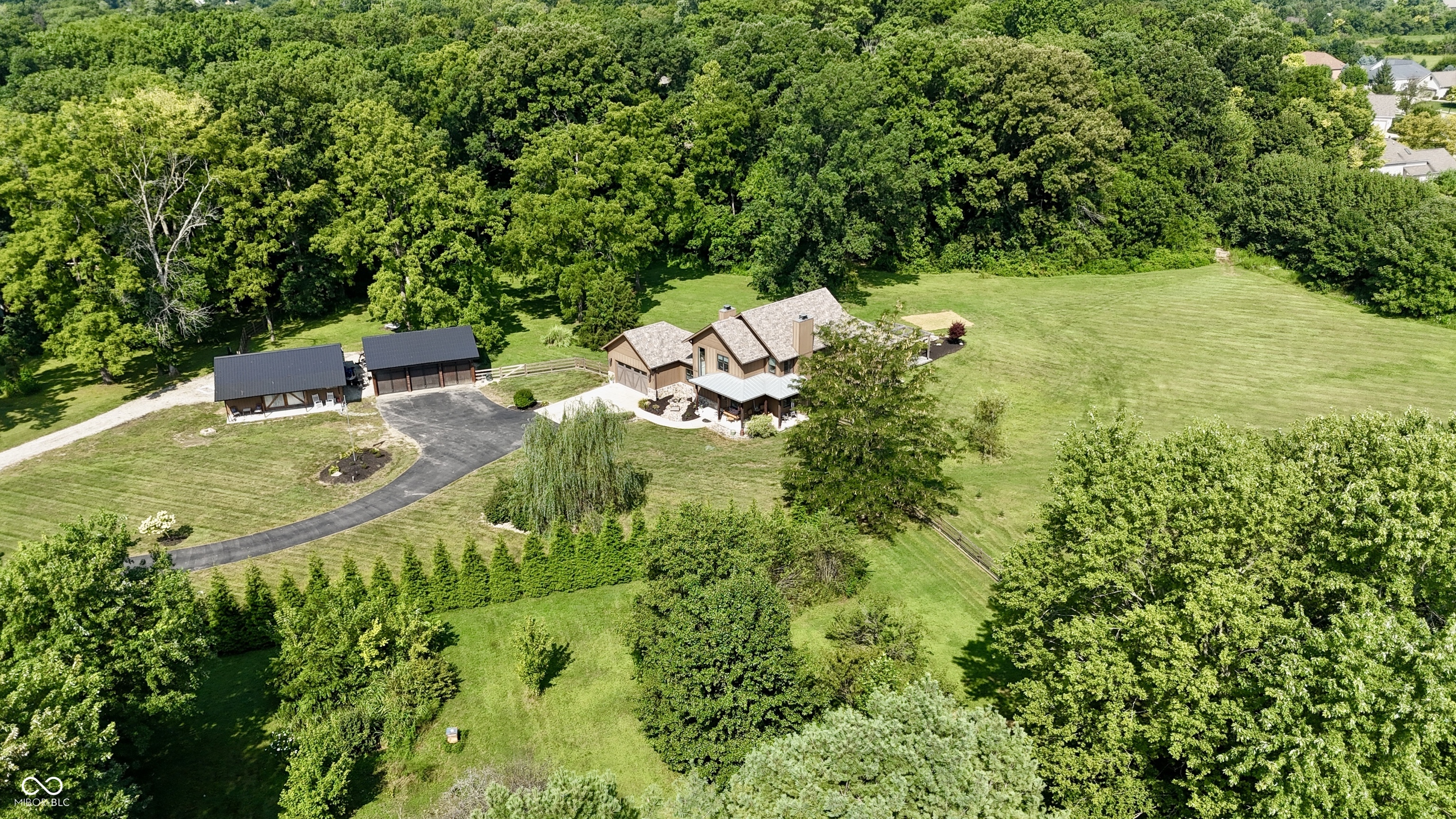Custom-built in 2018, this stunning home sits on 5 serene and private acres in Center Grove. Property offers 2 acres of woods, a 24x36 pole barn, and a detached 3 car garage with metal roof. Designed with attention to every detail, the gourmet kitchen features Kitchenaid appliances including built-in refrigerator, induction cooktop with pot filler, built-in microwave, separate ice maker, and a cast iron apron-front sink. Miller Maid cabinetry and custom lockers enhance the main-level laundry room.    Two wood-burning fireplaces anchor the main level, each with mantels reclaimed from Indiana's oldest tobacco barn. The main-level primary suite offers tray ceilings, a walk-in closet with California Closet design, a tiled walk-in shower, and a soaking tub. Upstairs, you'll find three bedrooms-one with a private bath and two connected by a Jack & Jill-as well as a loft.    The 9-foot-ceiling basement boasts two egress windows, an electric fireplace, gym, office, and a versatile craft room (or future bar). Systems include dual Bryant 19 SEER heat pumps, a 50-gallon heat pump water heater, and 400-amp service.    Outdoor living shines with a fully fenced backyard, stamped concrete patio with firepit, greenhouse, and an outdoor kitchen with built-in griddle, gas grill, and ice box. Relax in the hot tub with luxury seating under dusk-to-dawn lighting for both the exterior and stairwell. Real hardwood floors, thoughtful storage, and unique historic touches make this truly a one-of-a-kind property.