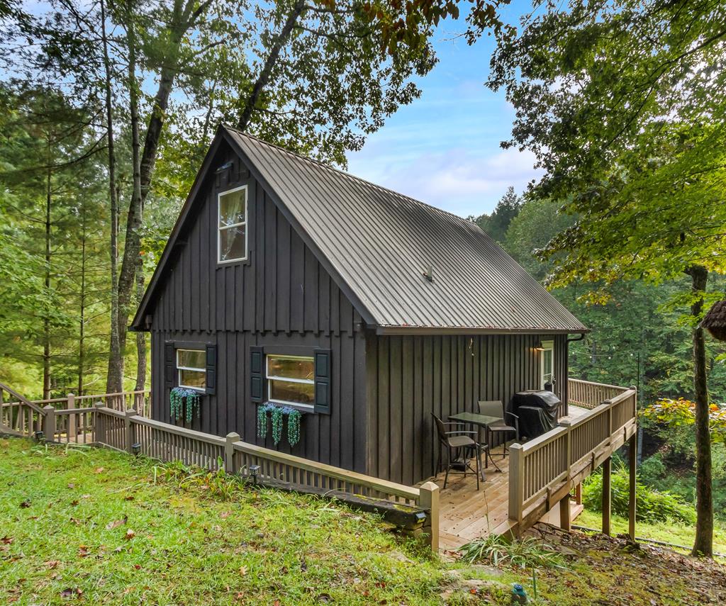 Discover the charm of mountain living in BEAR PAW RESORT in this fully furnished 3-bedroom, 2-bathroom cabin with a proven vacation rental history, on SEVEN LOTS totaling almost 2 acres. With board and batten wood siding, a durable metal roof, and a private, serene setting, this home offers the perfect blend of rustic style and modern convenience. A long, picturesque driveway leads you through the trees, with parking space for several cars at the cabin. Outdoor living is abundant, with decks that wrap around all four sides of the main level, a back porch on the lower level, and a fire pit for cozy evenings under the stars. Step inside to a warm, inviting kitchen with luxury vinyl flooring that extends throughout the main level. Stainless steel appliances, striking teal cabinets, and open shelving add a modern, stylish touch. A full bathroom is conveniently located just off the kitchen. The spacious Great Room has wood walls, a cozy fireplace, and double sliding glass doors that lead to the back deck overlooking the peaceful backyard. Upstairs, two large bedrooms with rich wood walls continue the rustic feel. The lower level, accessed by a spiral staircase, opens to a recreation room with a washer and dryer and another full bathroom. A barn door leads to the third spacious bedroom, which features sliding glass door access to the covered porch. Beyond the property itself, this home is located in Bear Paw Resort, a gated community known for its amenities and welcoming atmosphere. Owners enjoy access to a community pavilion, marina, basketball and tennis courts, paved roads ideal for biking or walking, and golf-cart-friendly streets. Add in the natural beauty of the mountains, the serenity of the lake, and a warm neighborhood feel, and you'll see why Bear Paw is considered one of the best hidden getaways anywhere.