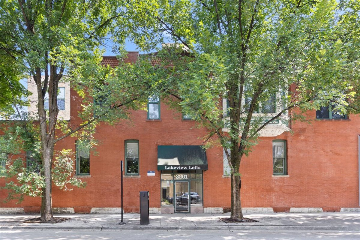 Big windows! Big character! Your own little corner of Lakeview. This sun-filled northwest corner loft brings together soaring 13-foot timber ceilings, exposed brick, and oversized 6- and 8-foot-tall windows framing leafy treetop views. Set back from neighboring buildings and facing away from Belmont, it has the open, airy feel that makes a true loft so special. The current owner has already tackled the big updates: a replaced washer and dryer, new hardwood floors in the lofted bedroom, refinished hardwood floors throughout, a beautiful gut-renovated bathroom, and a new kitchen island and countertop. You get to focus on the fun part-making it yours! The spacious living area is ready for lazy Sundays and a very ambitious plant collection. Huge corner windows and tall off-white drapes set the scene, while a wood-burning fireplace makes staying in an easy sell. The kitchen keeps everyone connected with an island offering built-in storage and room for stools, plus stainless steel appliances, a mix of white, frosted-glass, and stainless steel cabinetry, and a tall pantry cabinet. Upstairs, the lofted bedroom has nearly 15 feet of adjustable Elfa-organized closet space. An additional storage locker, bike storage, and your own outdoor parking space are included. Take the hangout upstairs to the large shared rooftop deck, where skyline views set the backdrop for grilling, catching up with friends, or unwinding after work. One block from the Belmont Red, Brown, and Purple Line station, with Lakeview's restaurants, coffee spots, shopping, and entertainment close by. The park and lakefront are a short walk away, too. Morning coffee, an easy commute, dinner out, or a bike ride by the water-there's a lot to love right outside your door.