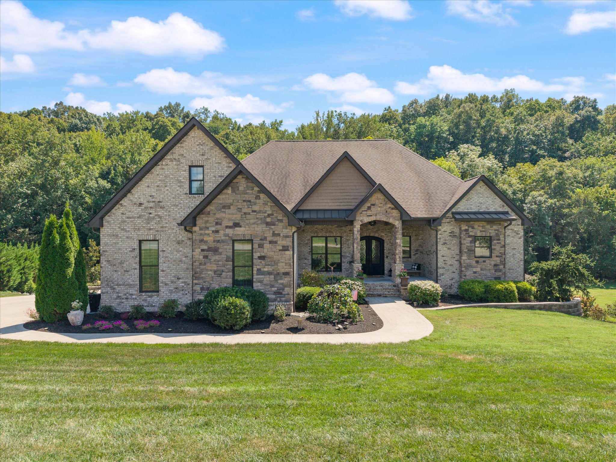 Distinguished, rare, and elevated—This custom-built estate offers approximately 4,780 square feet on over an acre, with 4 bedrooms and 3½ baths, showcasing exceptional craftsmanship and custom features throughout.  Distinctive Iron Lion double doors create a grand entrance, leading to a great room with 12-foot ceilings, 10-foot ceilings throughout, 8-foot solid wood doors, and extra-insulated interior walls. The gourmet chef's kitchen features Fisher & Paykel appliances, artisan-crafted cabinetry, farmhouse sink, expansive 8-foot granite island, custom coffee bar, and built-in dining-room serving station. Oversized laundry and mudroom, Signature wood blinds throughout the home, Minka Aire luxury ceiling fans and so much more!  The primary suite/owner's retreat, has a spa-like bath featuring heated floors, designer resin tub, and exceptional walk-in closet. The suite opens to a screened-in porch with fireplace, custom tongue-and-groove ceiling, and custom shades. The lower level delivers an extraordinary entertainment experience with an extra-large bedroom and bath, entertainment room with bar, bourbon lockers, In'finity-cooled wine room with slate floors and greenboard walls, plus a storm room and approximately 1,800 square feet of basement space.  Outside, a concrete-and-brick finished veranda extends from the polished tile sunroom. The exterior features professional landscaping, 1,000-gallon buried LP tank, Rain Bird irrigation with 8 zones plus drip system, and a private creek along the rear property line, creating a peaceful natural oasis. See attached Property Features for details.  Plenty of garage parking with a two-car garage with 10-foot insulated doors on the main level, traditional one-car lower-level garage. Every detail has been taken care of in this one---It's a must see!