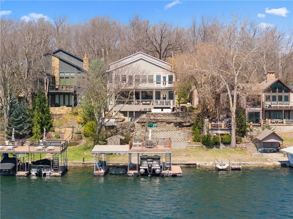 Experience exceptional lakefront living in this stunning main-channel home offering deep water and breathtaking views. Perfectly positioned with a double-well dock and boat lift and sun deck, this property is designed for both relaxation and recreation. The beautifully landscaped grounds lead to a thoughtfully designed home featuring a spacious 4-car garage and high-end finishes throughout. Inside, the gourmet kitchen boasts a walk-in pantry and flows seamlessly into a formal dining room and an impressive great room with a fireplace. The true showstopper is the wall of "moving glass wall", creating a completely unobstructed opening that blends indoor and outdoor living while showcasing the lake beyond. Step outside to a lakeside Trex deck spanning the length of the home, complete with a sunken hot tub, or unwind in the enclosed screened-in patio. The luxurious primary suite offers its own fireplace, private balcony with panoramic lake views, and a spa-like bath with separate vanities and a spacious closet. Two additional lakeside bedrooms provide incredible views and access to a screened-in deck, while a generously sized fourth bedroom above the garage offers added privacy. Designed for entertaining, the expansive family room that is ideal as a man cave or bunk room—features another fireplace, making it the perfect gathering space for family and guests. This is lake living at its finest.