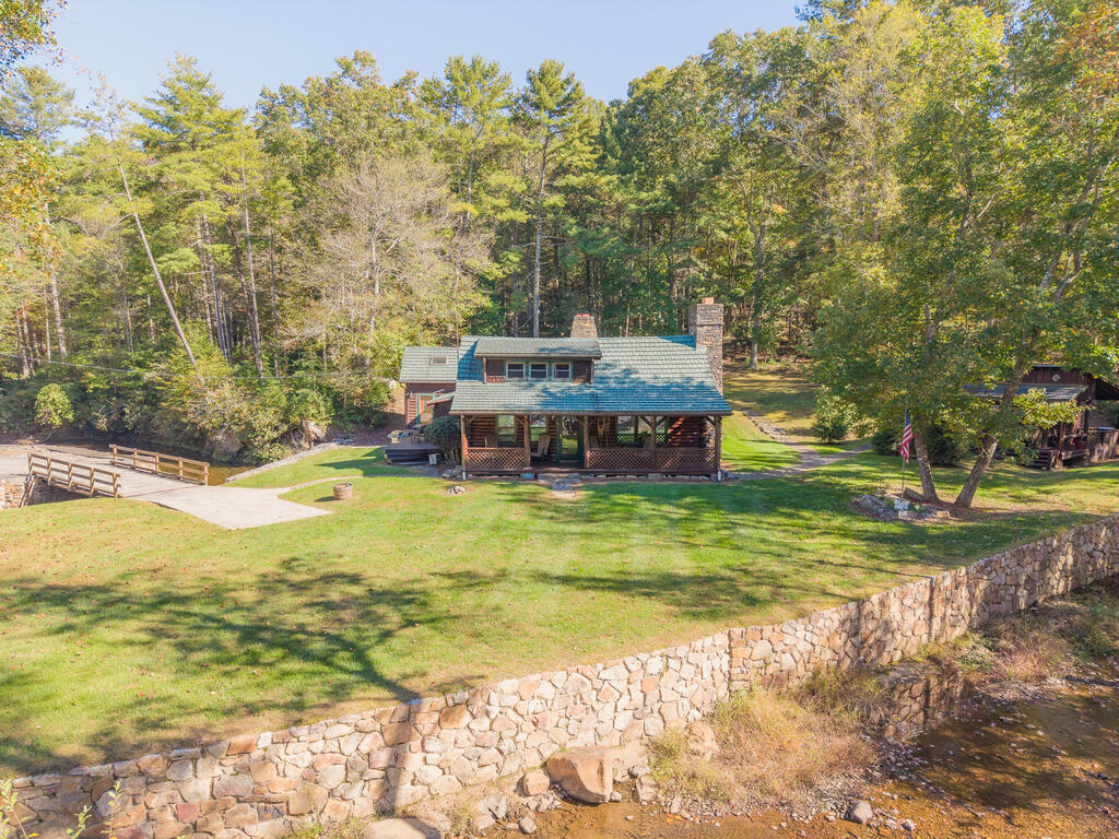 Discover an extraordinary private estate with a rich history, remarkable character, and endless possibilities. Previously owned by Wally Thrasher, this one-of-a-kind property offers approximately 50 acres of breathtaking natural beauty, bordering National Forest and featuring a stunning blend of wooded acreage, open fields, winding roads and trails, built walkways, and a beautiful private creek.  At the heart of the property is a distinctive main cabin/log home featuring 3 bedrooms, 3 bathrooms, a striking copper roof, custom details, and a spacious game room. Overlooking the beautiful creek, the home offers a unique combination of rustic charm, character, and peaceful surroundings. A detached two-car garage and workshop provide additional space for storage, hobbies, equipment, or projects.  The estate also includes two additional dwellings, creating exceptional flexibility and income potential. A charming one-bedroom, one-bath cottage and a separate one-bedroom, one-bath bungalow offer additional accommodations, with the bungalow already operating as an active Airbnb, providing an opportunity for continued short-term rental income.  With its combination of multiple dwellings, natural beauty, privacy, and established rental potential, this remarkable property offers an array of possibilities. Envision a private mountain retreat, an income-producing investment, a wedding or special-event venue, a hunting lodge, a family compound, or your own secluded oasis. Explore miles of roads and trails, wander through the wooded landscape, enjoy the open fields, or unwind beside the peaceful creek.  Properties offering this level of acreage, character, versatility, and proximity to National Forest are truly special. Whether you are seeking a unique investment opportunity, a destination property, or a private escape surrounded by nature, this exceptional estate invites you to create something extraordinary.