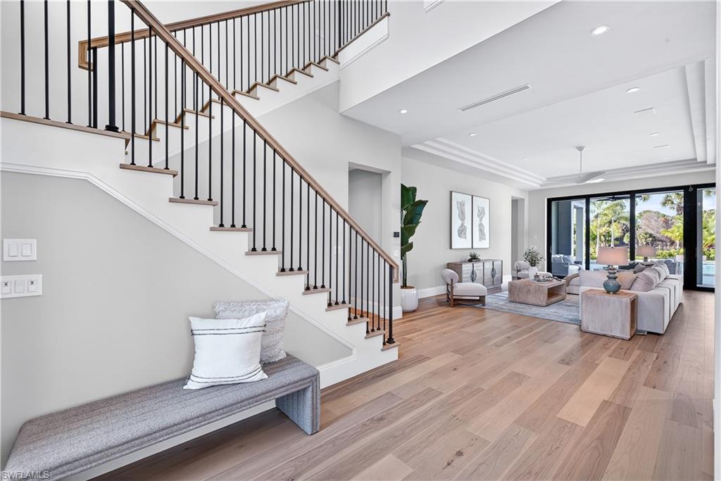 Living room with light wood-style flooring, a tray ceiling, recessed lighting, and a ceiling fan