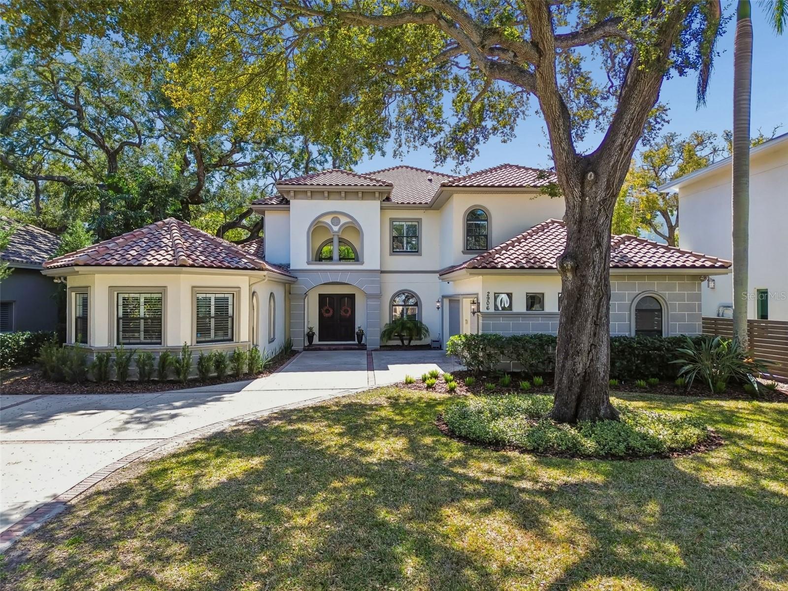 Located just four homes from Bayshore Boulevard on an 80 x 197 lot along one of South Tampa’s most desirable streets, this 2016 Bartlett Homes residence offers nearly 4,900 square feet of well-executed design, generous proportions, and exceptional natural light. The home feels expansive not only in size, but in volume, as soaring ceilings, large windows, and an open floor plan create a sense of space that is both impressive and comfortable. The main level balances formal and informal living with intention. A formal living and dining room greet you upon entry, while the central living space opens dramatically beneath 18-foot ceilings and is anchored by a gas fireplace and statement art wall. The kitchen is designed for everyday function and entertaining alike, featuring a large island with double-sided storage and seating, a gas cooktop, built-in microwave and oven, an Electrolux refrigerator, and a walk-in pantry with custom shelving and additional under-stair storage. The flow between the kitchen, living areas, and outdoor spaces is seamless. The first-floor primary suite offers privacy and scale, complete with custom shutters, a walk-in closet with built-in systems, and a spacious bath with dual vanities, a soaking tub, and a large walk-in shower with dual and rain shower heads. A secondary bedroom or office, a full pool bath, both with direct pool access complete the first level. Practical elements are thoughtfully integrated, including a mudroom with drop zone cabinetry, a full laundry room with utility sink, and a converted wine cellar now serving as additional custom storage. Upstairs, a wrought-iron staircase leads to a loft and separate media or game room, creating a natural second living area. Three additional bedrooms, all with hardwood floors, custom closets, and en-suite baths, provide privacy and flexibility. One bedroom opens to a private balcony through French doors. The outdoor living space is designed for year-round use, with a covered terrace overlooking a resort-style pool and spa, paver deck, and water features. The depth of the lot allows for meaningful backyard space, a rarity this close to Bayshore. Additional features include a three-car garage with epoxy flooring, four HVAC units, a tankless gas water heater, two electrical panels, a Rain Bird irrigation system service the home. Situated in Flood zone X, requiring no flood insurance, and high and dry during all past weather disruptions. This is a well-built, thoughtfully designed South Tampa home offering space, light, and exceptional proximity to Bayshore, downtown, Tampa International Airport, and the Gulf beaches