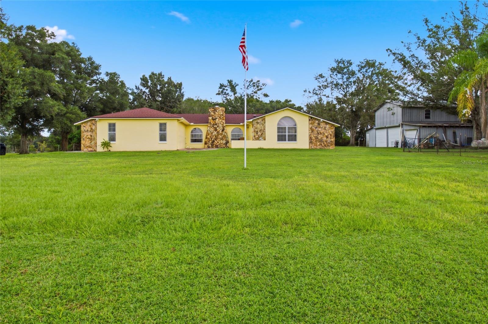 Discover the peace, privacy, and beauty of country living at 8634 23rd Street, Zephyrhills, FL. Situated approximately 160 feet above sea level atop a scenic hill, this unique property offers 4.89 acres of tranquil surroundings, rolling hill views, and western sunsets. This block home features an open floor plan, brand-new luxury vinyl plank flooring throughout, and a beautifully finished primary bathroom. Inside, a wood-burning fireplace creates a warm and inviting atmosphere, while the patio provides the perfect place to unwind and take in the spectacular sunset views across the surrounding hills. Beyond the home, the property offers an impressive, finished barn measuring over 1,100 square feet. With its versatile space, the barn presents exciting possibilities for a hobby space, workshop, guest retreat, or potential in-law suite or Airbnb conversion, subject to applicable zoning, permitting, and approval requirements. The acreage is thoughtfully equipped with a 20-by-20 water grid irrigation system to help support a variety of established and growing fruit plants and trees, including pomegranate, kiwi, berries, avocado, peach, fig, and plum. Whether you're dreaming of a peaceful homestead, a place to enjoy stunning sunsets, room to garden and grow your own fruit, or a property with flexible outbuilding potential, this Zephyrhills hilltop retreat offers a special combination of privacy, natural beauty, and opportunity. Come experience the views, the land, and the possibilities at 8634 23rd Street!