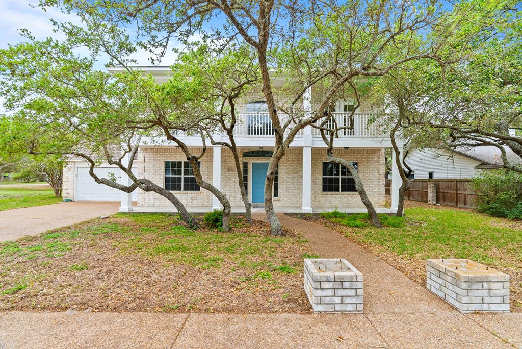 Tucked beneath a canopy of mature oaks is this stunning two-story home in Harbor Oaks. Move-in ready, it strikes the perfect balance between relaxed charm and refined living. Inside, the home opens into bright, welcoming spaces designed for both everyday comfort and effortless entertaining. Four generous bedrooms, three full bathrooms, two distinct living areas, and a formal dining room — or flexible bonus space — give every member of the household room to breathe. Fresh interior paint and new flooring throughout lend the home a crisp, contemporary feel while preserving its warm, inviting character. At the heart of the home is a well-appointed kitchen featuring expansive counter space, generous cabinetry, and a walk-in pantry that makes meal prep and hosting alike a pleasure. Large windows bathe the interior in natural light while framing peaceful views of the surrounding landscape. Step out onto the charming front balconies and let the oak-shaded breeze do the rest. The backyard is your private sanctuary — a concrete patio, dappled shade from towering oaks, and plenty of space to gather, grill, or simply savor a quiet morning coffee. As a Harbor Oaks resident, you'll enjoy exclusive access to a private boat ramp and fishing dock, making weekends on the water effortlessly within reach. All of this sits just minutes from Rockport's beloved shops, waterfront dining, and pristine beaches.