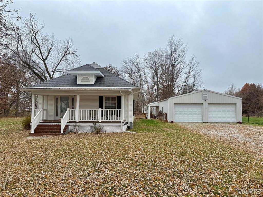 View of front of property featuring a porch, an outbuilding, roof with shingles, a garage, and a front yard