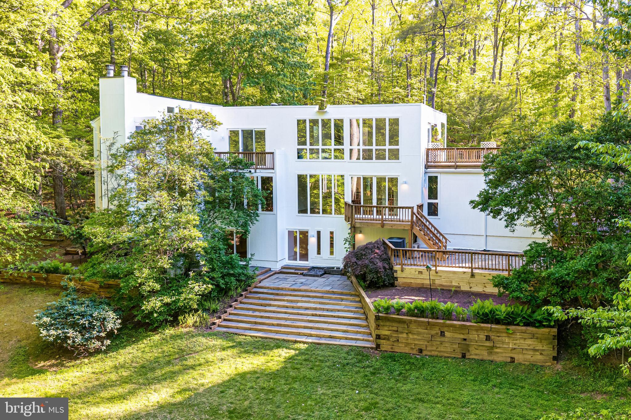 Welcome to 125 Eagles Mere Road, a striking contemporary residence offering 5 bedrooms, 5 full baths, and 1 half bath, set within a private Great Falls setting. Thoughtfully updated with new Pella windows and doors, Hardie Board siding, refinished wood flooring, and a renovated primary bath, the home presents a well-composed layout designed to capture its natural surroundings while supporting both everyday living and entertaining.  Inside, the main level unfolds with a series of connected living spaces defined by scale, light, and architectural detail. A two-story open staircase foyer introduces the home with a wall of windows. The living room offers an intimate gathering space with a wood-burning fireplace. The family room features a stone-faced fireplace with a beamed ceiling. The kitchen is designed for both function and gathering, featuring granite countertops, a full-height tile backsplash, oak cabinetry, and a center island with seating. The adjacent breakfast area is framed by skylights and windows, creating a bright and open setting, while the sunroom offers additional access to the deck and outdoor spaces. A main-level bedroom with en-suite bath and a private entrance from the deck provides flexibility for guests or single-level living.  Upstairs, the spa-inspired primary suite serves as a peaceful sanctuary, bringing the outdoors in through floor-to-ceiling windows and a spacious rooftop deck. The renovated primary bath features a custom dual-sink vanity, a soaking tub overlooking the trees, and a walk-in shower. Abundant windows and skylights fill the space with natural light, creating a serene, nature-filled setting. The suite is complete with a seating area and a walk-in closet. Additional bedrooms are thoughtfully arranged to accommodate a variety of living needs, including one with an en-suite bath and another with its own fireplace, while a full hall bath serves the remaining rooms. The lower level expands the home’s versatility with an exercise room, media room, recreation room, and full bath, along with multiple walk-out access points to the patio and backyard. These spaces provide options for entertainment, fitness, or additional living needs while supporting the home’s overall functionality.  Easy indoor-outdoor living is integrated throughout the property, with resealed decks on all sides of the home, multiple patio areas, and a layout that connects to the surrounding landscape bordering Potomac River regional parkland. Additional updates include new exterior lighting and gutters, enhancing both the home’s presentation and maintenance.  Located within the Langley High School pyramid and close by to Great Falls Village, Riverbend Park, Potomac River trails, and major commuter routes, the home offers convenient access to Tysons, Reston, and the surrounding region while maintaining a private residential setting.  This is a home designed for both everyday living and gathering, where space, light, and setting come together in a cohesive and well-executed design.