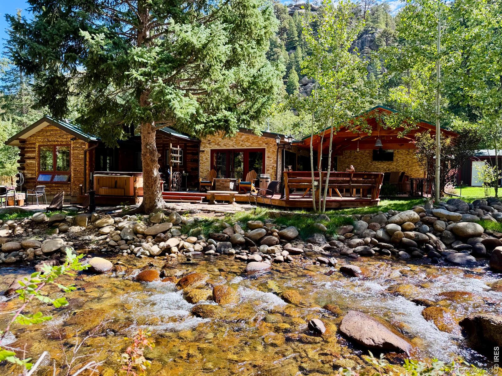 Where mountain charm meets a little bit of magic! This special 4-season waterfront home in the Raymond area of Lyons beautifully blends the character of its 1925 roots with thoughtful updates and an outdoor setting that feels like your own private retreat. Offering 3 bedrooms, 2 bathrooms and an abundance of outdoor living on .44 acres. The property features approximately 200' of riverfront along the spectacular backyard. Step outside and the fun really begins! The beautifully landscaped yard features expansive decks, a flagstone patio, and an impressive 25' x 22' covered patio with 4 skylights, decorative stone walls, built-in electric fireplace and TV-perfect for morning coffee, evening gatherings or simply listening to the river flow by. Inside, the large picture windows capture the views of the property in every room. The living room steals the show with a wood-finished cathedral ceiling, copper skylights, exposed wood beams and a cozy woodstove. The remodeled kitchen brings together rustic Colorado style and modern function with a farmhouse apron sink, 6-burner gas range, stainless appliances, butcher-block counters, custom brass backsplash and radiant-heated flooring. Additional features include an oversized 1-car garage, 35' x 10.5' carport, 20.5' x 8.5' shed on a permanent foundation, 500-gallon propane tank, whole-house water softener on well water, and an electrical interlock/transfer switch for a full-house generator. A rare opportunity to own a home with history, heart, mountain views and a backyard where the river practically becomes part of the property. Come discover your own little slice of Colorado magic!