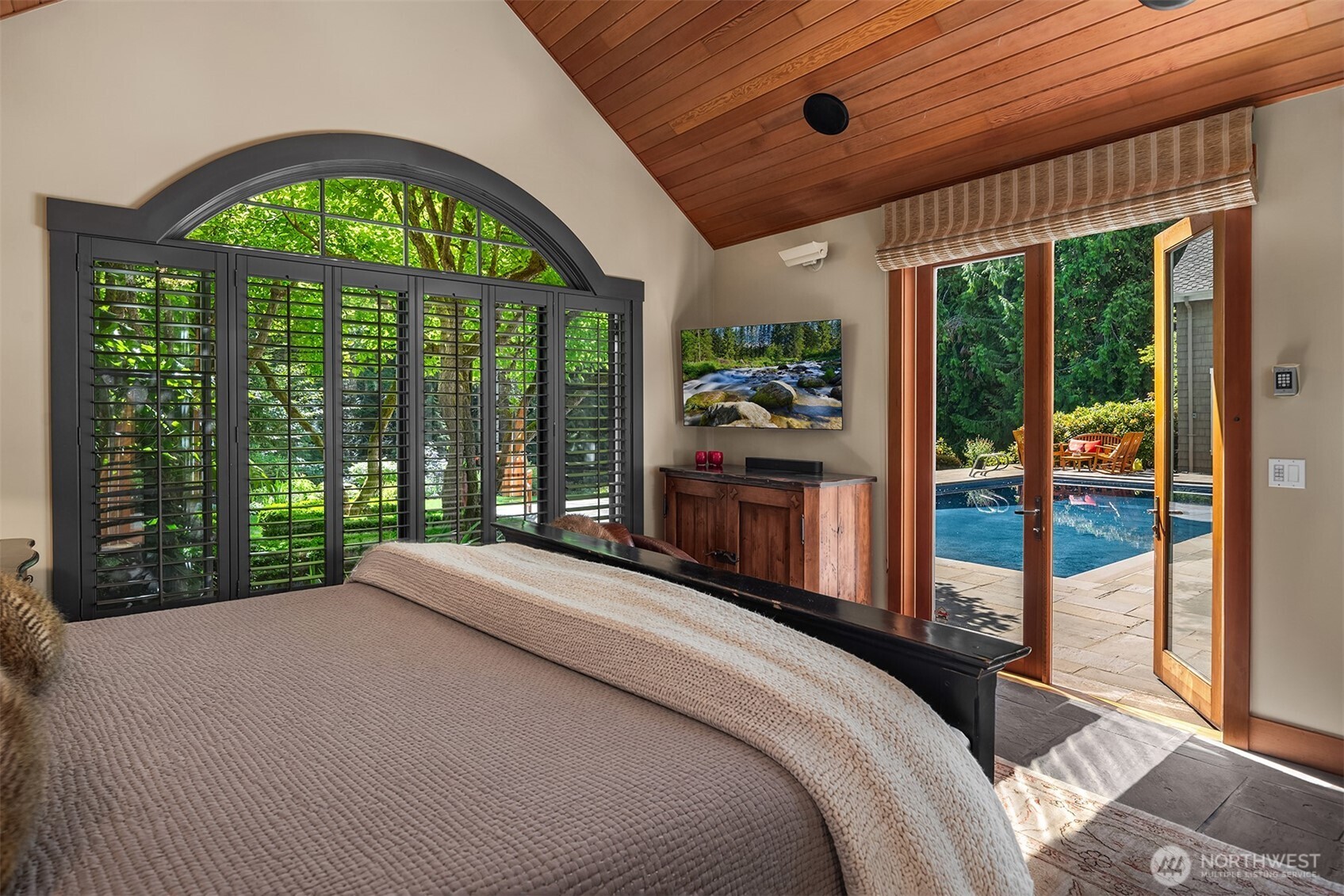 Bedroom with arched shuttered window, wall-mounted TV, and door to pool patio