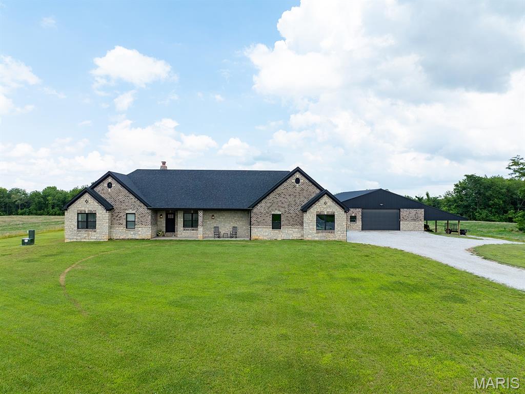 French country inspired facade featuring driveway, a front yard, stone siding, and a chimney
