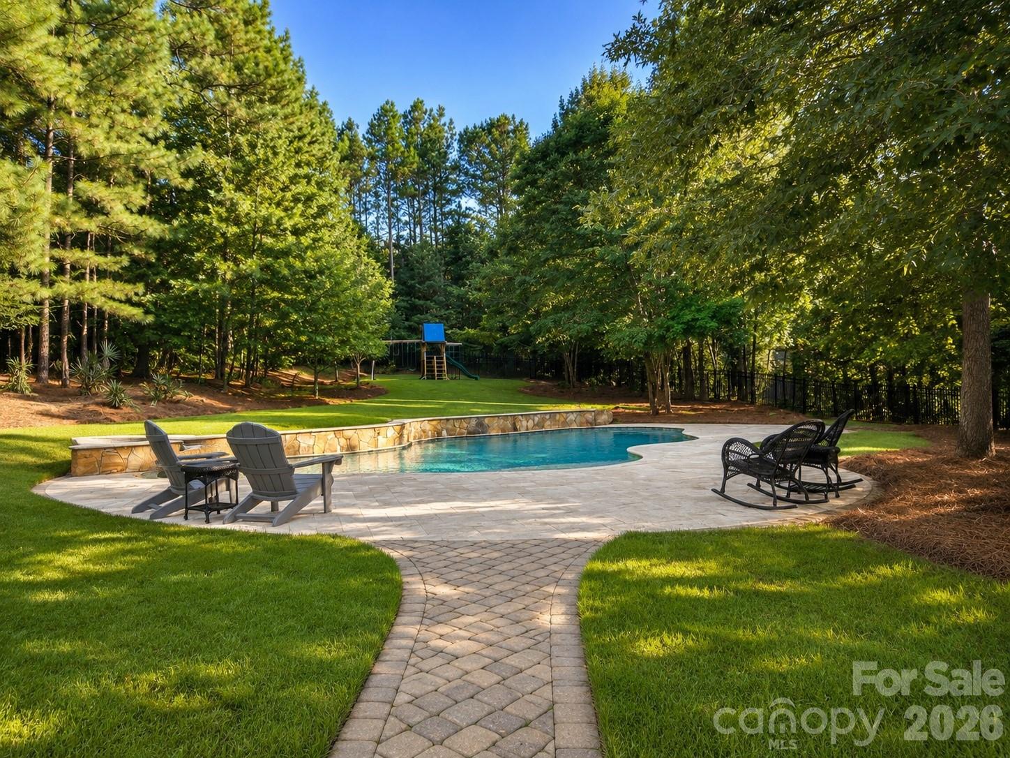 Welcome home to your own private retreat. Set on 1.45 fenced acres surrounded by mature trees, this custom home was designed to capture the beauty of its setting. Walls of oversized windows frame the resort-style backyard from the great room, kitchen, breakfast area, and primary suite, creating views that become part of everyday living. Whether you're enjoying your morning coffee, gathering with family, or watching the seasons change, the connection between the home and its surroundings is something truly special.The backyard is designed for year-round enjoyment with a custom pool and spa, expansive paver patios and walkways, fireplace, outdoor kitchen, large fenced lawn, and wooded privacy. It's equally suited for entertaining a crowd or enjoying a quiet evening at home.Inside, a grand two-story foyer opens to an executive office with floor-to-ceiling wood paneling and stone fireplace, a formal dining room with a stepped tray ceiling, and a two-story great room featuring a wall of arched windows and a see-through fireplace shared with the keeping room.The gourmet kitchen serves as the heart of the home with custom cabinetry, granite countertops, stainless steel appliances, 6 burner gas stove, decorative vent hood, walk-in pantry, and a large island with seating. Open to the breakfast area and keeping room, the layout flows naturally to the screened porch and outdoor living spaces.The main-level primary suite offers a private retreat with a stepped tray ceiling, fireplace, sitting area, and backyard views. The en-suite bath features separate vanities, a jetted soaking tub, tiled walk-in shower, private water closet, and a custom walk-in closet with built-in cabinetry, drawers, shelving, and shoe storage.Additional features include Brazalian hardwood floors throughout the main living areas and upstairs hallway, extensive crown molding and millwork, coffered and tray ceilings, multiple fireplaces, a screened porch, three-car garage, and generous secondary living spaces. Located just minutes from new Harris Teeter, shopping, dining, and top-rated Fort Mill Schools including Catawba Ridge HS, this home offers the privacy of an estate setting with the convenience of Fort Mill living.Homes with this level of privacy, outdoor living, and connection to nature are rarely available. Every room was thoughtfully designed to take advantage of the setting, creating a home where everyday life feels a little more peaceful and every gathering feels a little more memorable.