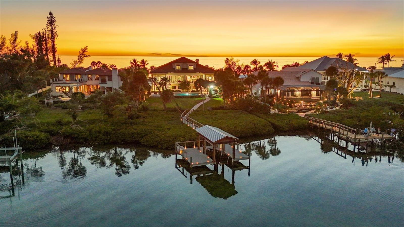 Set along one of Casey Key’s most coveted stretches, 3210 Casey Key Road presents a rare Gulf-to-Bay estate where water defines nearly every moment of daily life. Enjoy your private beach with rare, grandfathered cabana and your private bay frontage with dock and irreplaceable covered boat lift. Spanning almost 5,400 square feet under air across three-plus levels, this 2018-built residence offers four bedrooms, four full baths, a powder bath, multiple living and bonus spaces and, last but not least, an indoor half basketball court, all framed by impact-rated glass and serviced by a three-stop elevator. Arrival begins through a lushly landscaped circular motor court leading to a coastal-inspired façade and a covered entry accented by wood inlay ceilings. Inside, engineered wood floors, crown molding, and curated architectural details introduce interiors that balance sophistication with warmth. The dining room captures Gulf views through an oversized window, while the library doubles as a refined retreat with beamed ceilings, built-ins, a fireplace, and French doors opening to a Gulf-facing terrace. At the heart of the home, the great room unfolds around a stone-clad fireplace and opens through Euro-wall glass doors to expansive outdoor living. The chef’s kitchen is both beautiful and highly functional, anchored by two oversized islands and finished with quartz countertops, tile backsplash, custom cabinetry, and a premier appliance suite including Wolf, Sub-Zero, Miele, and Vent-A-Hood. A walk-in pantry with additional prep space, a light-filled breakfast nook overlooking the bay, and a well-appointed laundry room complete the main living level. Two private primary suites on the main floor offer exceptional flexibility, each opening to terraces with pool and Intracoastal views. One features a steam shower and tailored walk-in closet, while the other is styled as a spa retreat with chandelier-lit marble finishes, a freestanding soaking tub, and a custom-designed dressing room. Upstairs, a lounge-style bonus room with wet bar and Gulf views creates an ideal gathering space, accompanied by two guest suites, both enjoying tranquil Intracoastal outlooks. The expansive lower level introduces remarkable versatility, with bonus living areas including a dedicated craft room and extensive storage rarely found in coastal homes. An indoor half-court basketball court makes this amenity driven property even more interesting. Outside, the estate truly comes into its own. A heated saltwater infinity-edge pool and spa anchor the backyard, complemented by an outdoor kitchen, pergola with gas firepit, outdoor shower, and pass-through bar for effortless entertaining. A Trex boardwalk leads to the dock and rare and irreplaceable covered boat lift, offering direct Gulf-to-Bay boating with no fixed bridges. On the beach side, a grandfathered cabana is the perfect venue for enjoying specular everyday sunsets. Situated on approximately 0.82 acres, the property provides both scale and privacy, framed by mature landscaping and sweeping water views on both sides. Set on the serene barrier island of Casey Key, this Gulf-to-Bay estate offers effortless access to boating, beach, and the dining and cultural scenes of Venice and Sarasota. More than a home, 3210 Casey Key Road is a refined coastal retreat where sophisticated interiors, resort-style amenities, and exceptional waterfront living come together.