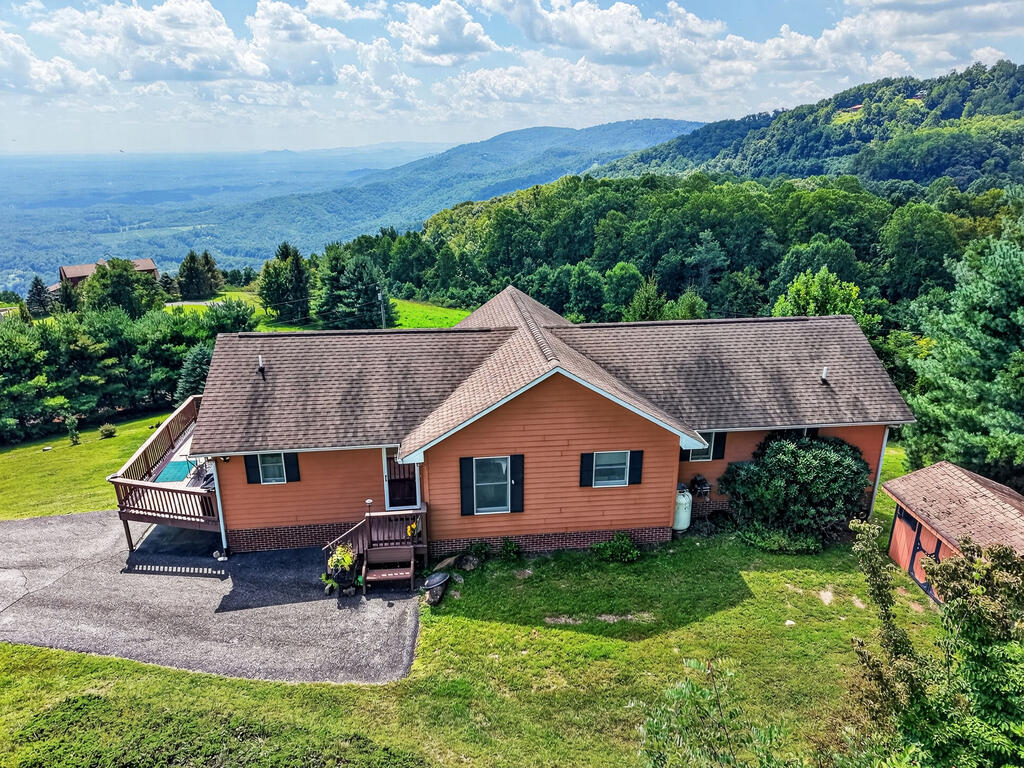 Breathtaking long-range mountain views, exceptional privacy, and a fascinating local history come together in this one-of-a-kind retreat! Tucked away in a small, private gated community, this impressive home sits on a 1-acre corner lot and showcases panoramic views stretching all the way to Winston-Salem, Pilot Mountain, and Mount Airy. A massive deck spans the entire length of the home and wraps around the side, creating the perfect setting for morning coffee, entertaining, or simply soaking in the scenery. The walk-out basement opens to a full-length patio featuring a hot tub hookup and porch swing for even more outdoor enjoyment.  Inside, the main level offers an inviting open-concept living, dining, and kitchen area with vaulted ceilings and a wall of windows designed to capture the spectacular views. Beautiful hardwood floors flow throughout the main level, which includes 3 bedrooms, 2 full bathrooms, and laundry. The expansive lower level is an entertainer's dream, featuring a massive great room with soaring ceilings, a stunning stone gas-log fireplace, kitchenette, space for a pool table and games, and room to gather with family and friends. A spacious guest room with its own full bathroom provides excellent privacy for visitors, while a large workshop/storage room offers abundant flexibility.  Adding a truly special touch to this property, the home was once owned by well-known local author C. David Gelly, who wrote all of his books here. A rare opportunity to own a private mountain retreat with unforgettable views, generous living space, and a story of its own!