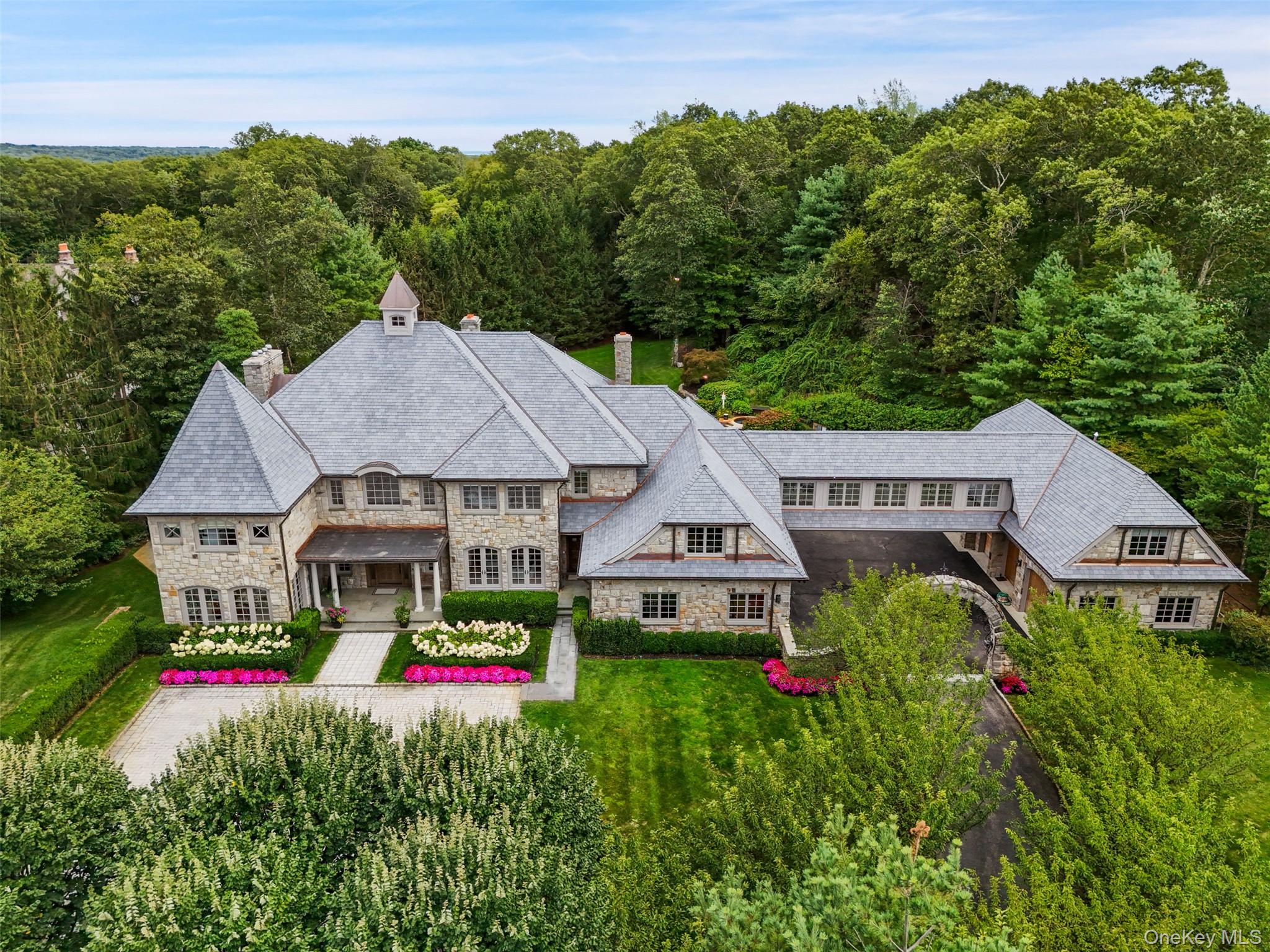 Set majestically on nearly three gated acres in Armonk’s coveted Wrights Mill Estates, this extraordinary hand-cut stone manor with over 12,000 sq ft of classic architecture, artisan craftsmanship, and resort-caliber living. A breathtaking foyer leads to the two-story great room with an impressive window wall and fireplace.  A richly paneled study and sunlit conservatory offer space for dual home offices. A family room, dining room, chef’s kitchen with pantry and breakfast room, complete the main level. The upper level offers a grand primary suite, a luxurious retreat featuring a fireplace, dual spa baths, separate dressing rooms, and a third-floor private wellness space with sauna. Additionally, upstairs, four ensuite bedrooms, laundry room and den are joined by a dramatic enclosed bridge leading to a private guest wing. The lower level rivals a private club with lounge, wet bar, wine cellar, theater, gym, hot yoga studio, bedroom, bath and second laundry. Outdoor amenities are designed for both relaxation and entertaining, featuring a beautifully integrated pool, an independent spa, expansive terraces and patios and a built-in outdoor grill. The flat, beautifully manicured grounds are complemented by an elegant courtyard with eight garage bays providing generous space for prized automobiles and collections alike. Combining timeless-inspired grandeur with modern luxury, this remarkable estate presents a rare opportunity to enjoy a private country-club lifestyle just minutes from downtown Armonk and Greenwich, with convenient access to New York City. A truly exceptional opportunity for the most discerning buyer.