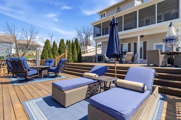 Nestled in a desirable cove on Bandit Bay, this immaculately maintained first-tier lakefront home blends timeless Cape Cod charm with modern updates. Offering 4 bedrooms and 3 full baths, it features light-filled, functional spaces designed for comfortable lake living. The living room centers around a cozy fireplace and flows into the kitchen with white cabinetry, quartz countertops, updated finishes, and white oak flooring throughout the main level. A dining area just off the kitchen provides comfortable space for everyday meals and gatherings. The main-level primary suite offers convenience and privacy. A screened porch connects the kitchen and primary suite, creating a relaxing space for morning coffee or lake views. The walkout lower level features LVP flooring, a spacious family room with fireplace, laundry area, and a fourth bedroom with full bath, ideal for guests or additional living space. Outdoor living shines with an expansive deck offering multiple seating areas, plus a hot tub and firepit area perfect for entertaining or relaxing by the water. The newer two-tier dock is a single-well powder-coated steel design built for function and enjoyment. It includes kayak racks, a 10’x24’ slip with HydroHoist boat lift, PWC lift, wireless speakers, and dock boxes. Recent updates include a home renovation in 2021, HVAC , dock and hot tub in 2022, and hot water heater in 2025, offering peace of mind. Ample parking includes a two-car garage plus driveway space for guests. The 2015 21’ tritoon and 2023 jet ski are available separately, along with select furnishings, making this a turnkey opportunity. Located in the Lake Lotawana community with easy access to Hwy 7 and 50, residents enjoy boating, jet skiing, fishing, swimming, and a vibrant community with yacht club, ski club, tennis and pickleball courts, and Marina 27 nearby. Move-in ready and just a short drive to Lee’s Summit and Kansas City, ideal as a full-time residence or weekend retreat.