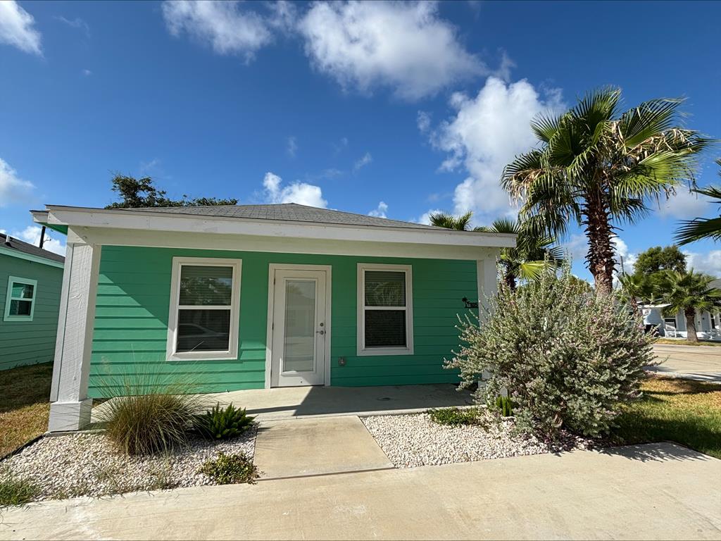 Charming turquoise house with palm trees and landscaping, showcasing a welcoming front entrance in Rockport, Texas, ideal for real estate listings.