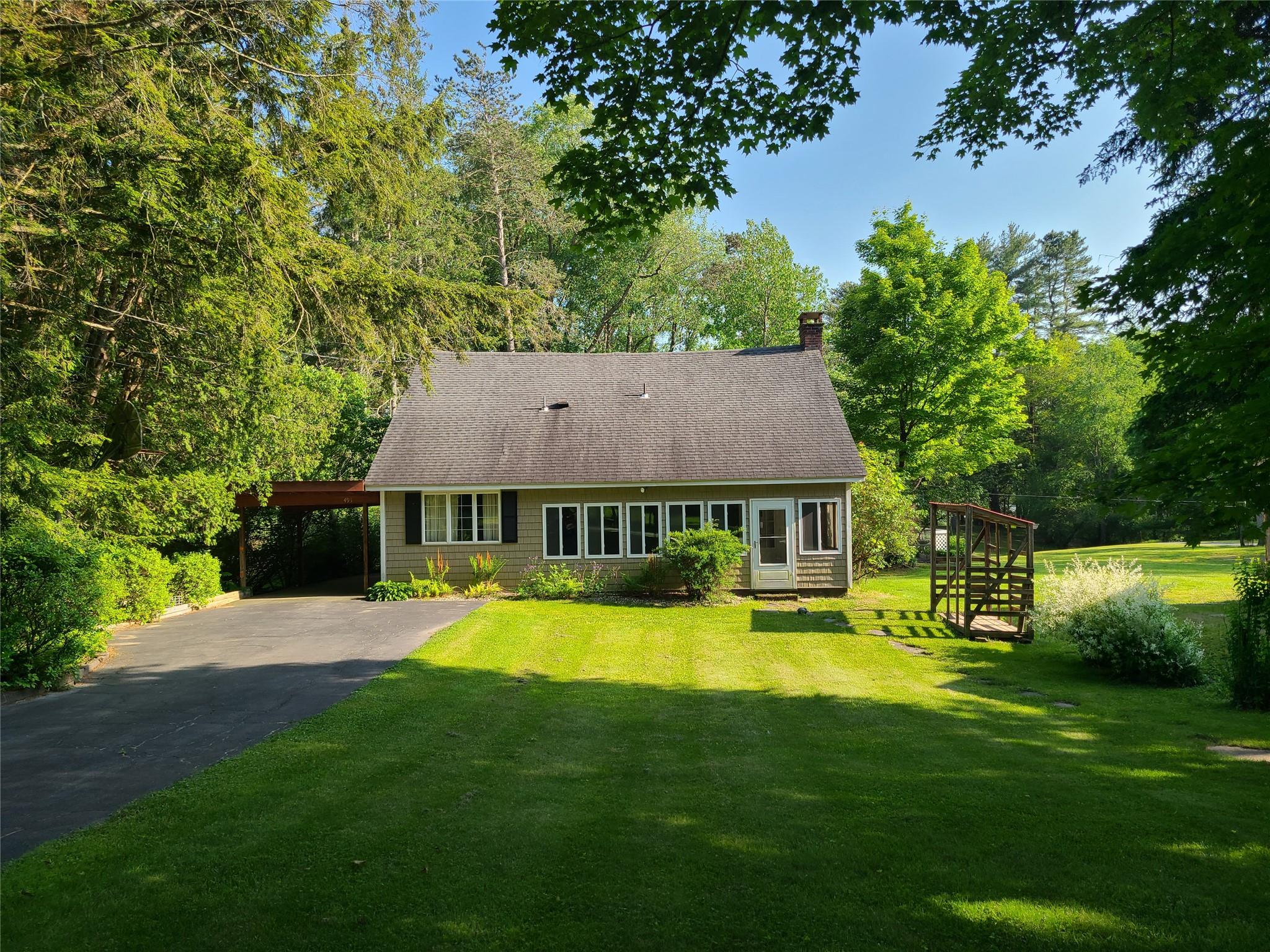 View of front of house featuring driveway, a front lawn, a chimney, a carport, and a shingled roof