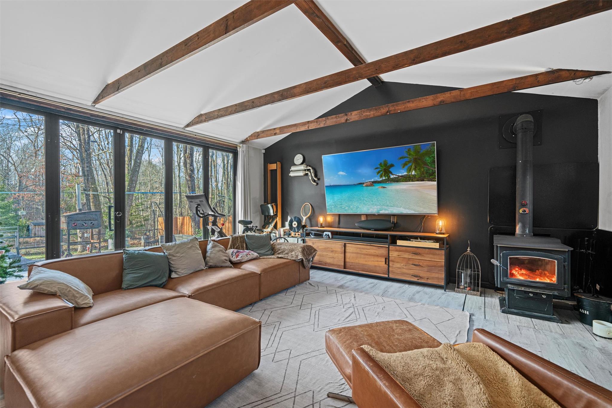 Living room featuring a wood stove, light carpet, and vaulted ceiling with beams