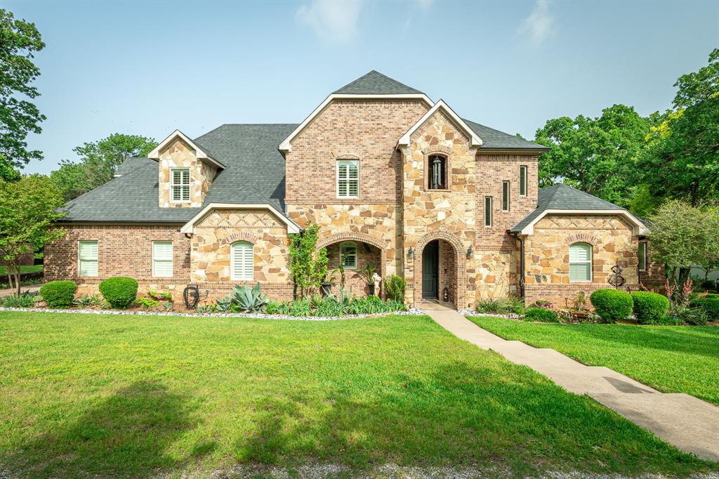 Welcome to 700 Coffee Circle! A masterfully crafted luxury estate located in the prestigious Millers Subdivision of Pottsboro, TX, just moments from the shimmering shores of Lake Texoma. Set beneath a canopy of mature trees with stunning lake views, this 3,374 sq ft custom home is a rare blend of architectural elegance, resort-style outdoor living, and timeless craftsmanship. Step through the dramatic arched entry into a grand two-story foyer where soaring ceilings, rich hardwood stair treads, and wrought iron balusters set the tone for everything that follows. The breathtaking two-story great room commands attention with walls of oversized windows flooding the space with natural light, a stunning stone fireplace as its centerpiece, and an open flow into the gourmet kitchen and granite bar making this the ultimate space for both everyday living and grand-scale entertaining. Retreat to the first-floor primary suite, a true sanctuary featuring private French doors opening directly to the outdoor living area. The spa-inspired primary bath offers dual vanity stations with granite countertops, a step-up soaking tub, and a separate shower. Three additional bedrooms provide comfort and privacy for family and guests, each with its own private full bath. Step outside and discover one of the most distinctive outdoor living spaces in the region. This sprawling covered brick patio is anchored by a one-of-a-kind stacked-stone outdoor fireplace. Lush landscaping and the peaceful sounds of nature surround you, creating an outdoor escape that blurs the line between inside and out. Located in the sought-after Millers Cove community, it's a short walk to the four mile hiking trail or the small beach area for a quick swim, and is minutes from Little Mineral, Lighthouse, and Highport Marina offering effortless access to boating, fishing, swimming watersports, and all that Lake Texoma has to offer. This is more than a home. It is a lifestyle. Come experience it for yourself.