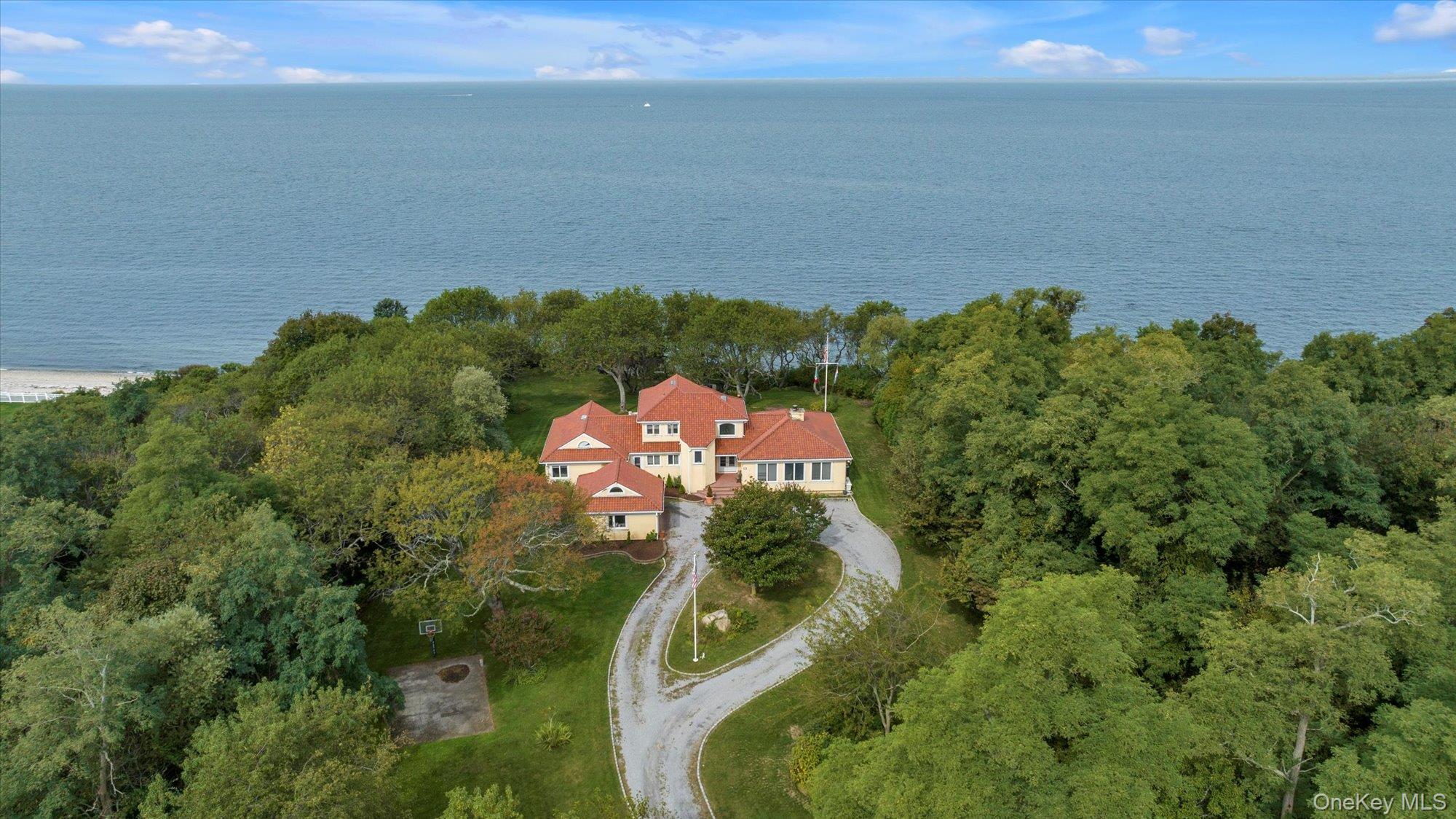 Welcome to your private sanctuary on Long Island’s North Fork. This striking Mediterranean-inspired residence sits on over 2 acres of lush, water-front property, accessible only by driving through a working farm.  Ensuring both exclusivity and a bucolic sense of arrival.
As you approach, a winding drive sets the tone, with pastoral vistas and mature landscaping revealing the home gracefully perched near the water’s edge. The exterior features classic stucco and terracotta details that evoke timeless Mediterranean architecture. Step inside to a warm and inviting interior, where abundant natural light pours through expansive windows framing serene waterfront views. The main level offers an open living and dining area, ideal for both entertaining and daily living.  One of the home’s standout assets is the finished lower level, perfect as a recreation hub, media room, or flexible living space to suit your lifestyle.  Outside, the grounds are spectacular, sweeping lawns and multiple terraces lead you down toward the water’s edge. Whether enjoying morning coffee while listening to gentle lapping waves or hosting al fresco dinners under the stars, this property offers truly magical moments.