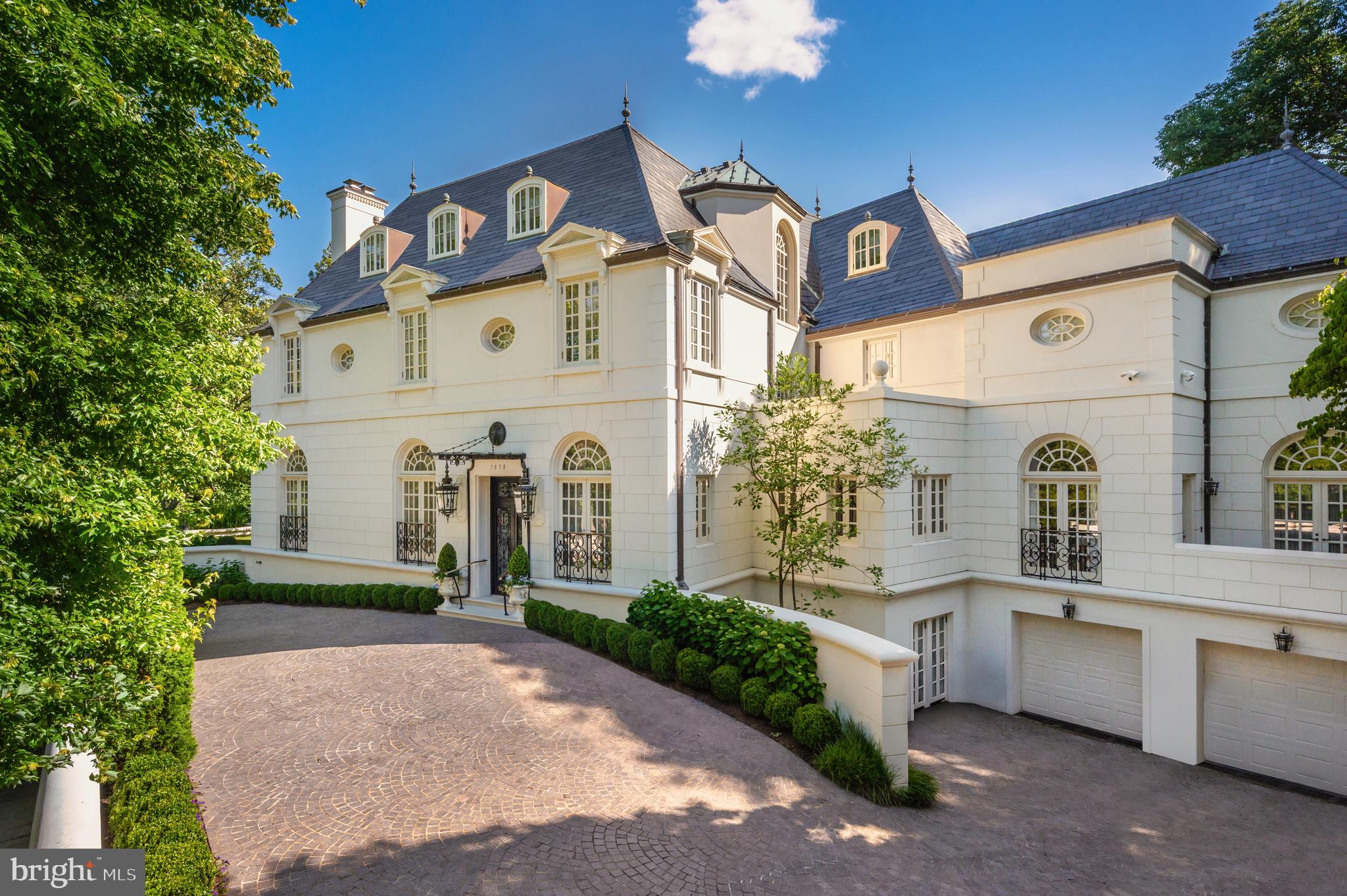 Nestled in the heart of prestigious, leafy Massachusetts Avenue Heights, 2838 McGill Terrace NW is the quintessential Washingtonian mansion. Originally designed by esteemed architect John W. Kearney and constructed in 1931 with a bygone standard of craftsmanship, the estate is a fortress of timeless luxury.Sited on an exceptionally large 0.47-acre lot, a low wall discreetly conceals a gracious heated cobblestone crescent driveway, offering a resplendent first impression. Arched Palladian windows set deep into the white stucco façade, a steep slate roof, and an elegant glass-and-wrought-iron portico flanked by oversized lanterns evoke a distinct French Provincial sensibility. Intricate double wrought-iron doors open into an arched entry vestibule, richly adorned with hand-painted murals. Beyond, the grand foyer reveals itself — herringbone floors, soaring ceilings, and an illuminated sweeping staircase immediately impress. Elaborate plasterwork crowns the main level, where formal entertaining spaces radiate from the central foyer, creating an effortless flow for gatherings both grand and intimate.Each formal space is lavishly appointed with handcrafted millwork, ornate fireplaces, and multiple sets of French doors that seamlessly invite the outdoors in. Both the formal living and dining rooms span nearly 30 feet in length, offering banquet-scale proportions rarely found today. A spacious butler’s pantry links the dining room to the chef’s kitchen, equipped with redundant commercial-grade appliances and commanding views of the rear lawn. A charming breakfast room with indoor/outdoor flow and a richly paneled study complete the main level.Upstairs, a luxurious primary suite is accessed through double doors and overlooks the manicured rear grounds. A central dressing room connects three expansive walk-in closets to dual marble-clad primary baths, each boasting luxuries such as sunken tubs, walk-in showers, and bespoke vanities including a dedicated cosmetics counter. Three additional bedrooms, each with walk-in closets and ensuite baths, complete this level. The top floor offers three more bedrooms, two with ensuite baths, while a third shares a hall bath with a bonus room, ideal for a playroom or study.The lower level hosts a large recreation room with direct access to the temperature-controlled two-car garage. An eighth bedroom suite, perfect for an au pair, accompanies a spacious laundry room, walk-in safe room, and a mirrored fitness center. Surrounded by retaining walls and fully enclosed, the estate’s parklike grounds are whimsical and masterfully curated. Extensive landscaping and hardscaping create a harmonious balance of open lawns and intimate garden spaces. A sweeping granite terrace wraps around the rear façade, while the centerpiece — a magnificent 36-foot private swimming pool — lies beyond, hidden by an extended trellis wall and lush canopy.Around the corner from the Omni Shoreham and steps from Embassy Row, 2838 McGill Terrace NW occupies one of Washington’s most desirable addresses. Evoking the essence of a grand Washington estate, it stands as one of the city’s most distinguished residential offerings.